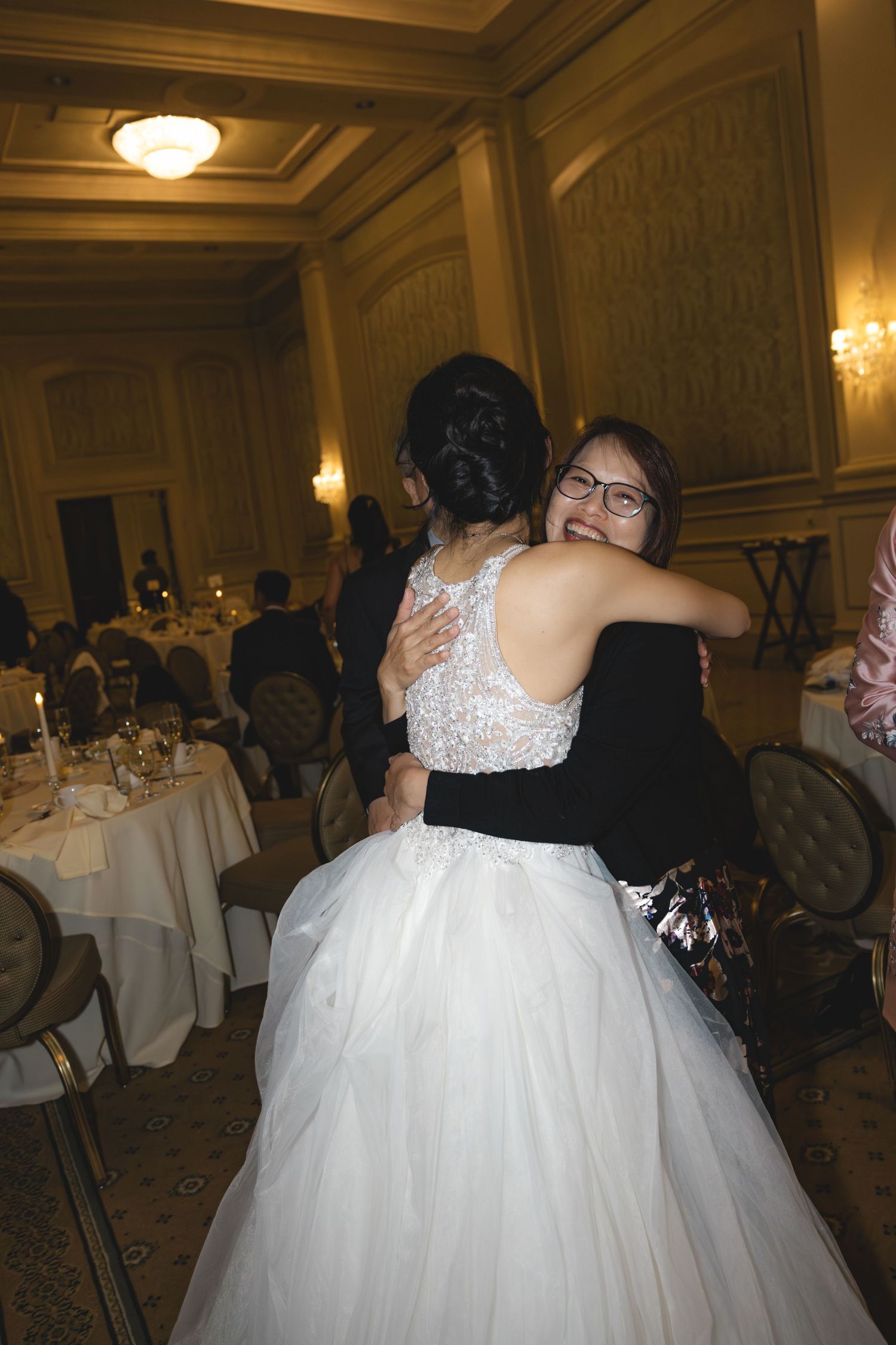 Bride sharing a warm hug with a smiling wedding guest at reception.