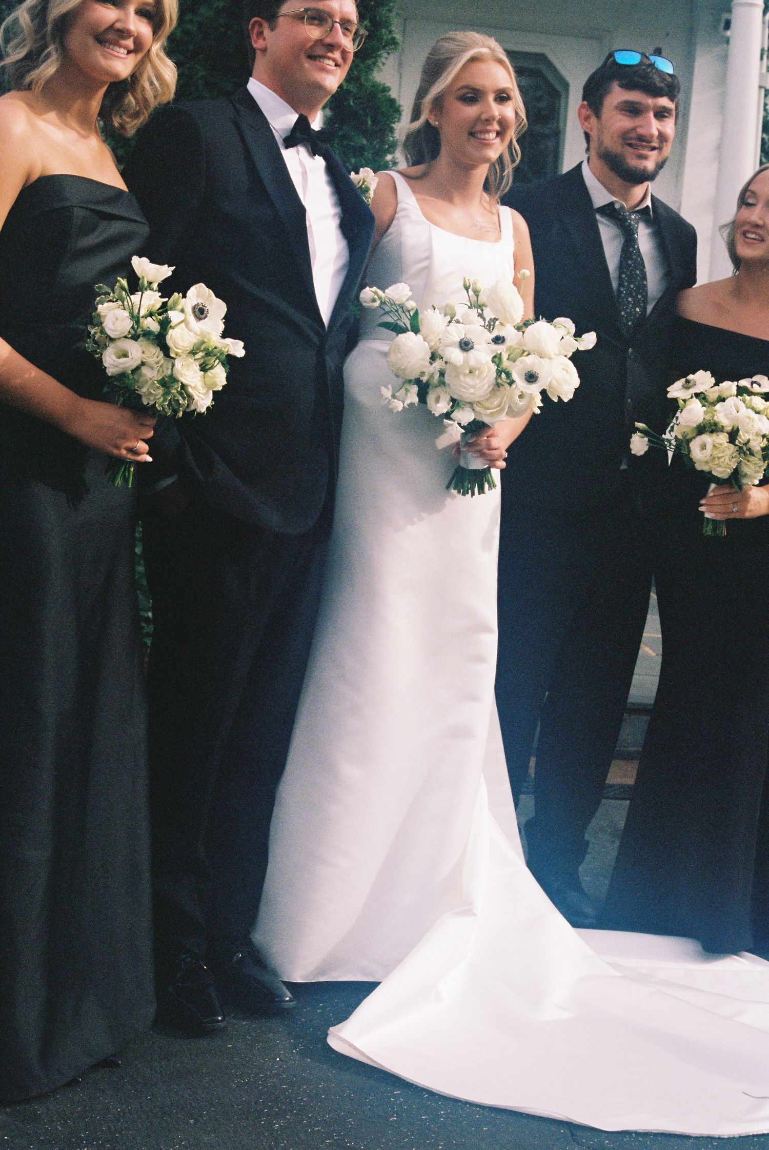 A formal wedding party poses for a photograph, with the bride and groom standing in the center surrounded by their wedding party.