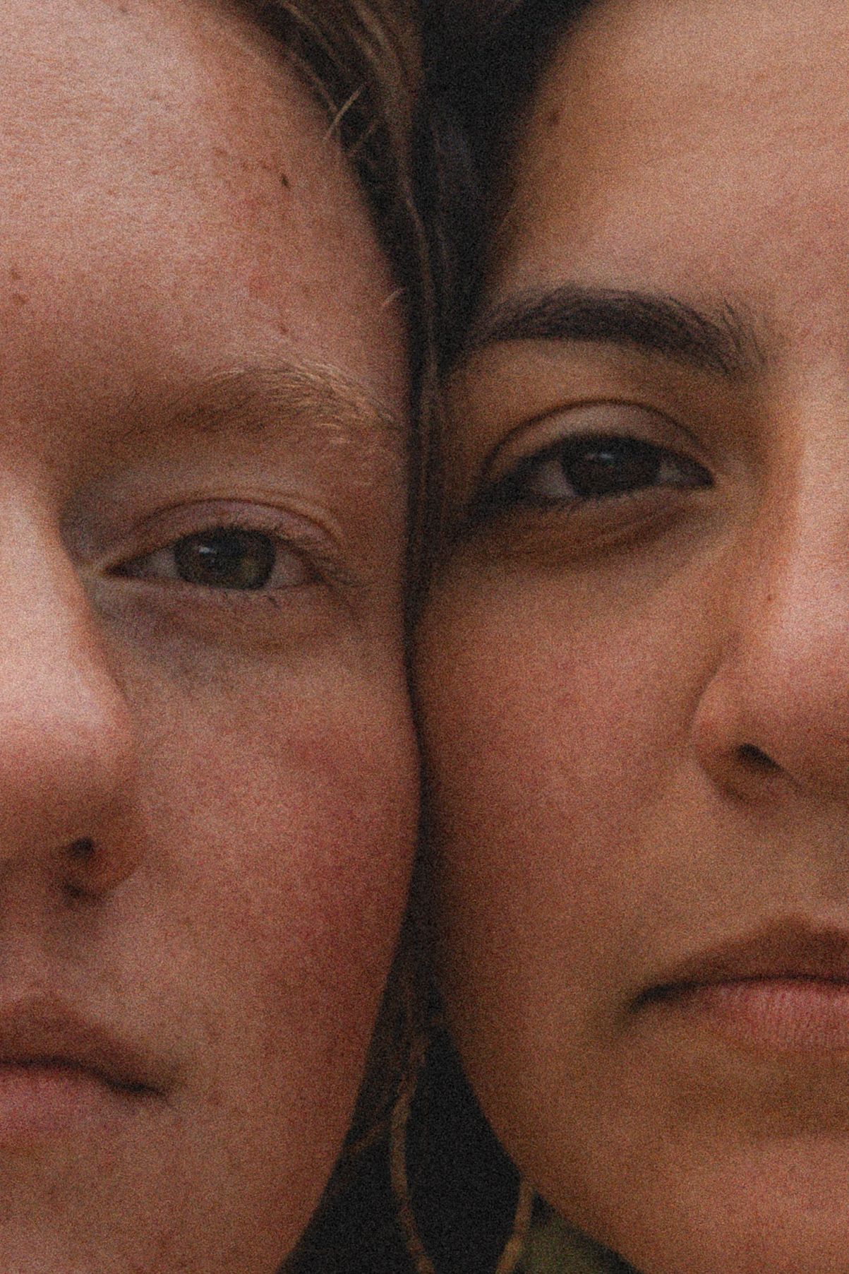 Close-up portrait of two young women with heads together, showcasing diverse skin tones and natural beauty.