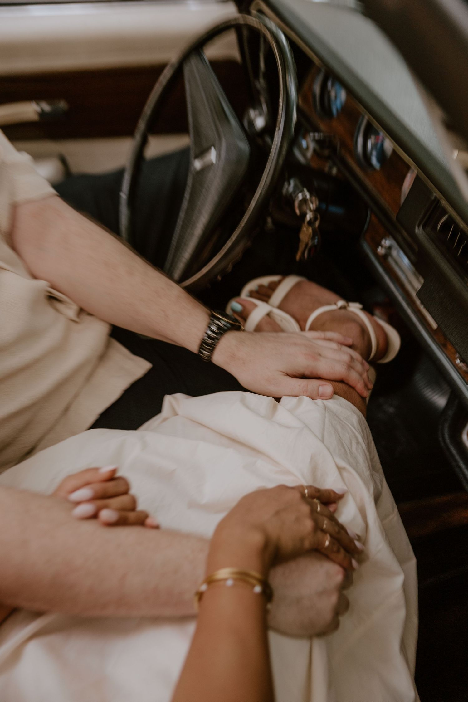Two hands clasped together on a car seat with vintage interior details visible.