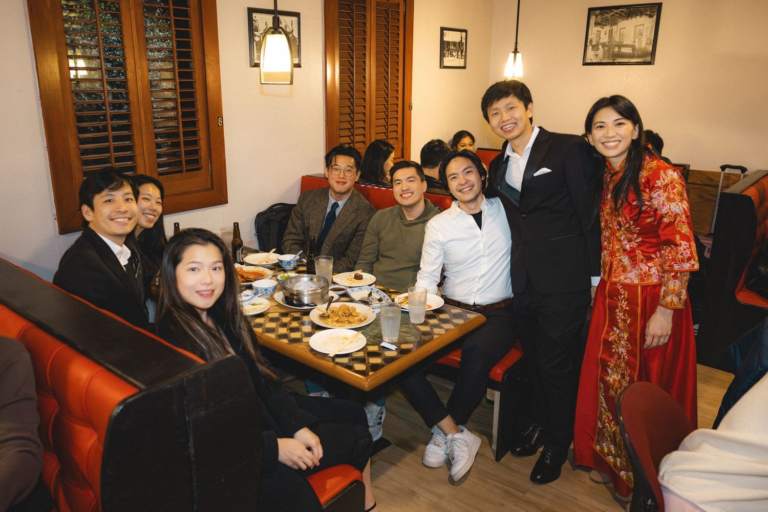 Group of elegantly dressed Asian family members posing together at a Chinese restaurant dinner table celebration.