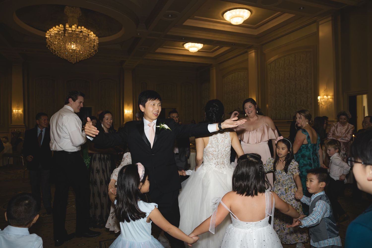 Bride and groom dancing with guests and children at wedding reception.