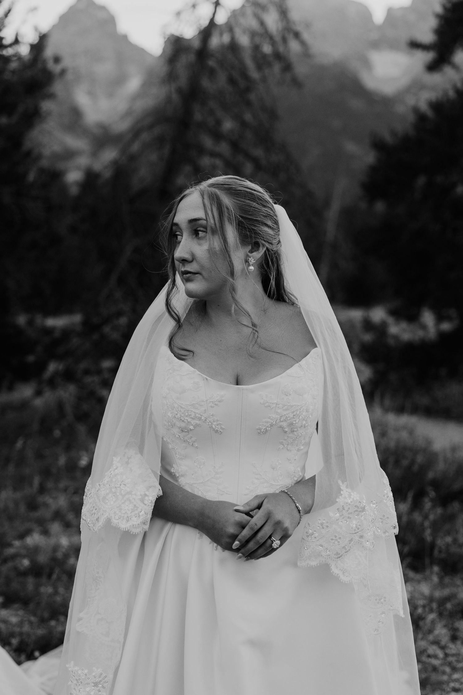 Black and white bridal portrait of a bride in a lace wedding gown and veil with mountain scenery.