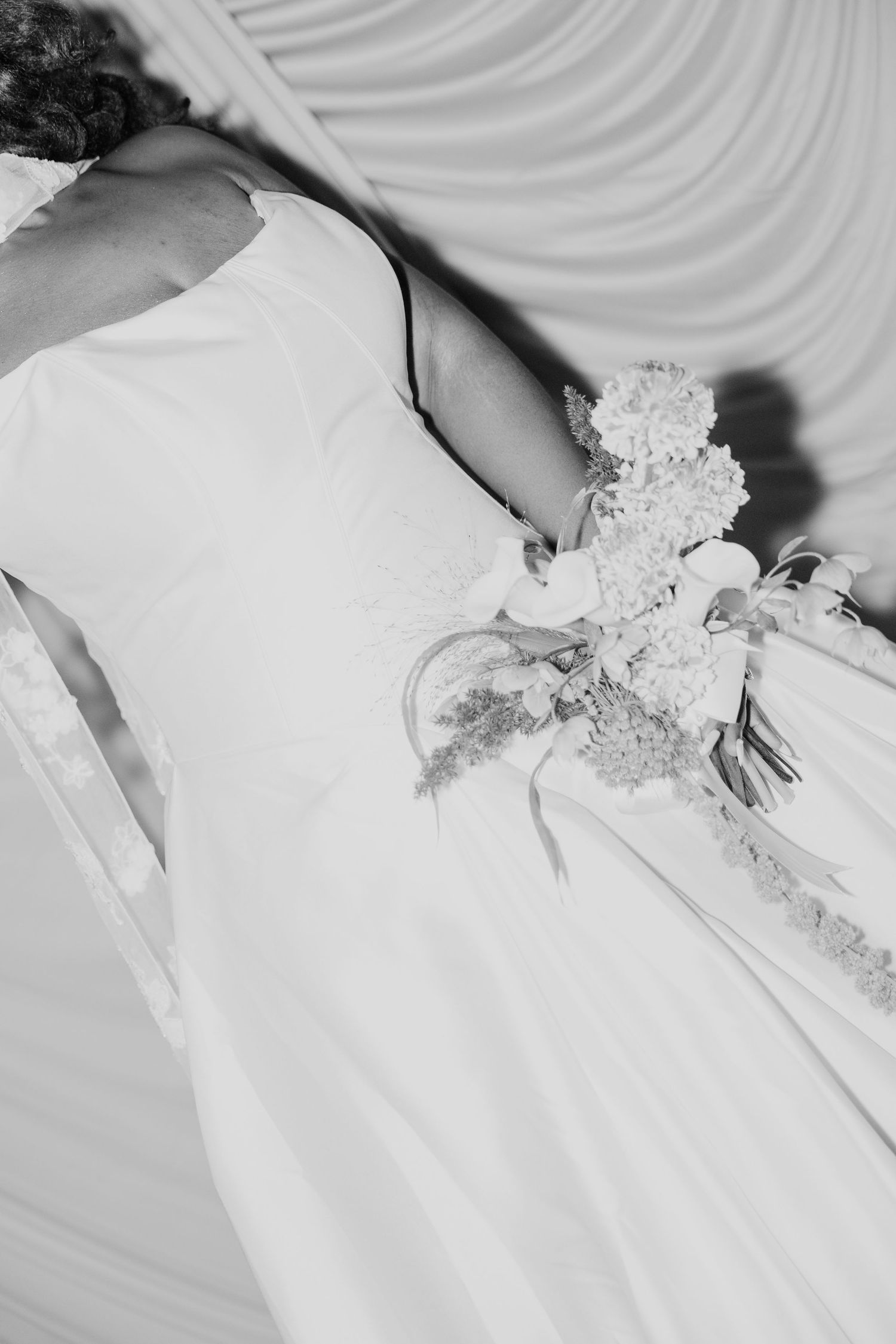 Black and white photo of a bride in a white wedding gown holding a floral bouquet at her side.