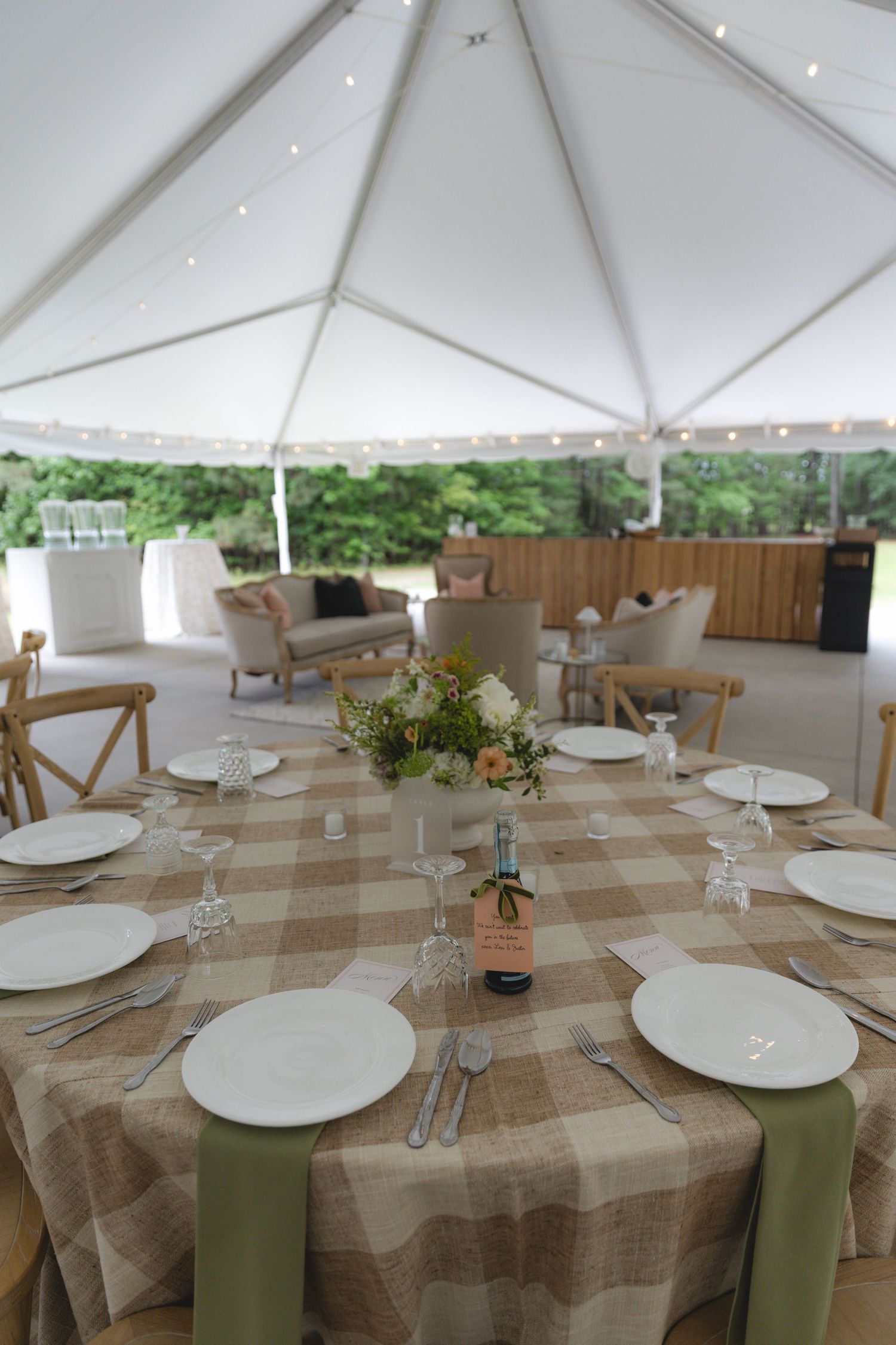 Elegant tented wedding reception with plaid tablecloths, white plates, and mini champagne centerpieces.