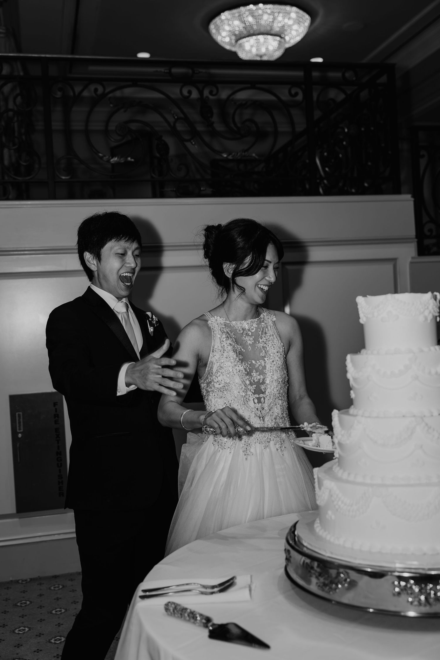 Bride and groom laughing while cutting their elegant tiered wedding cake at their reception.