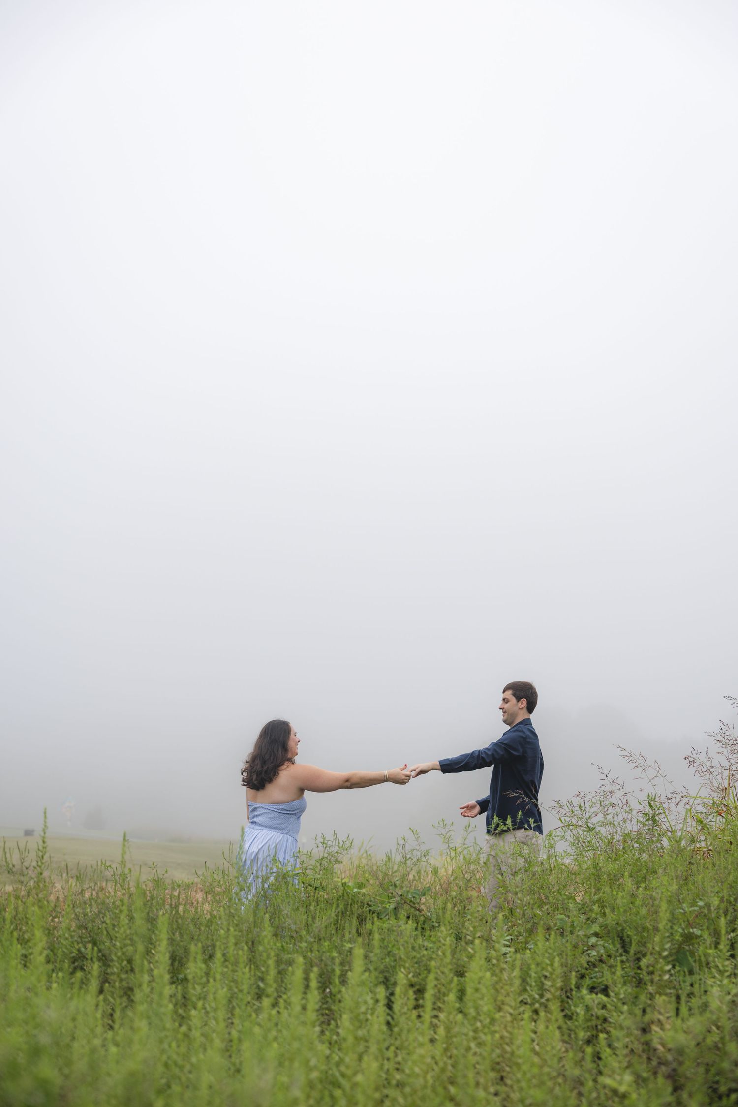 Couple holding hands in a misty field surrounded by green wildflowers on a foggy day.