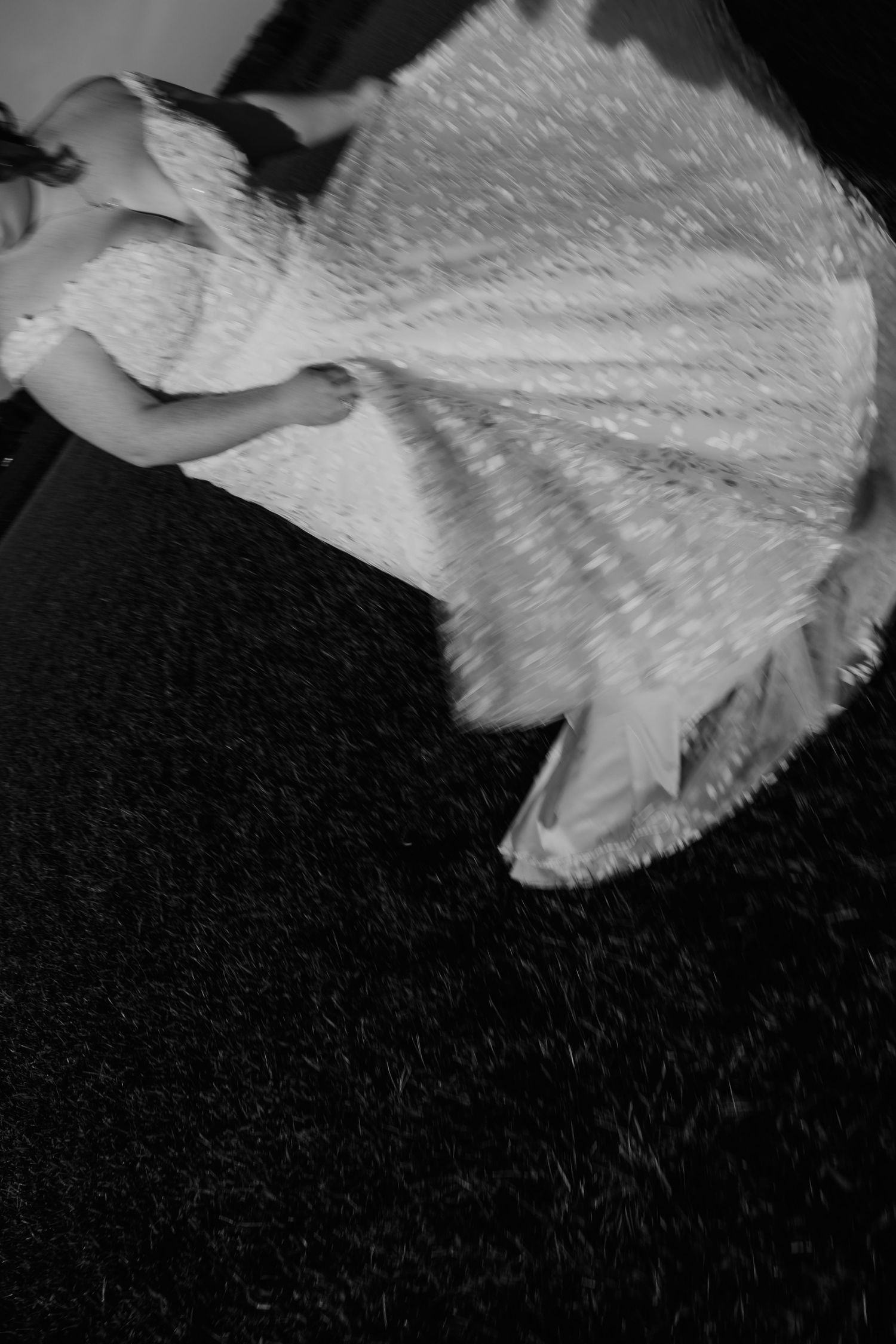 Black and white photo of a woman in a flowing white ball gown spinning on a dark dance floor.