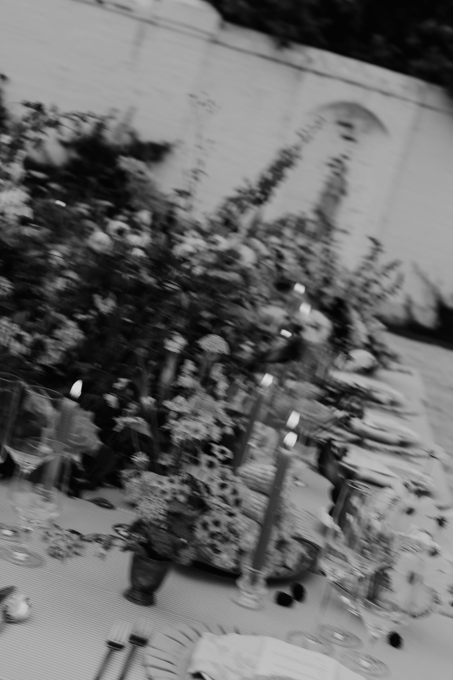 Black and white photo of an elegant outdoor wedding reception table with lush floral arrangements and candles.