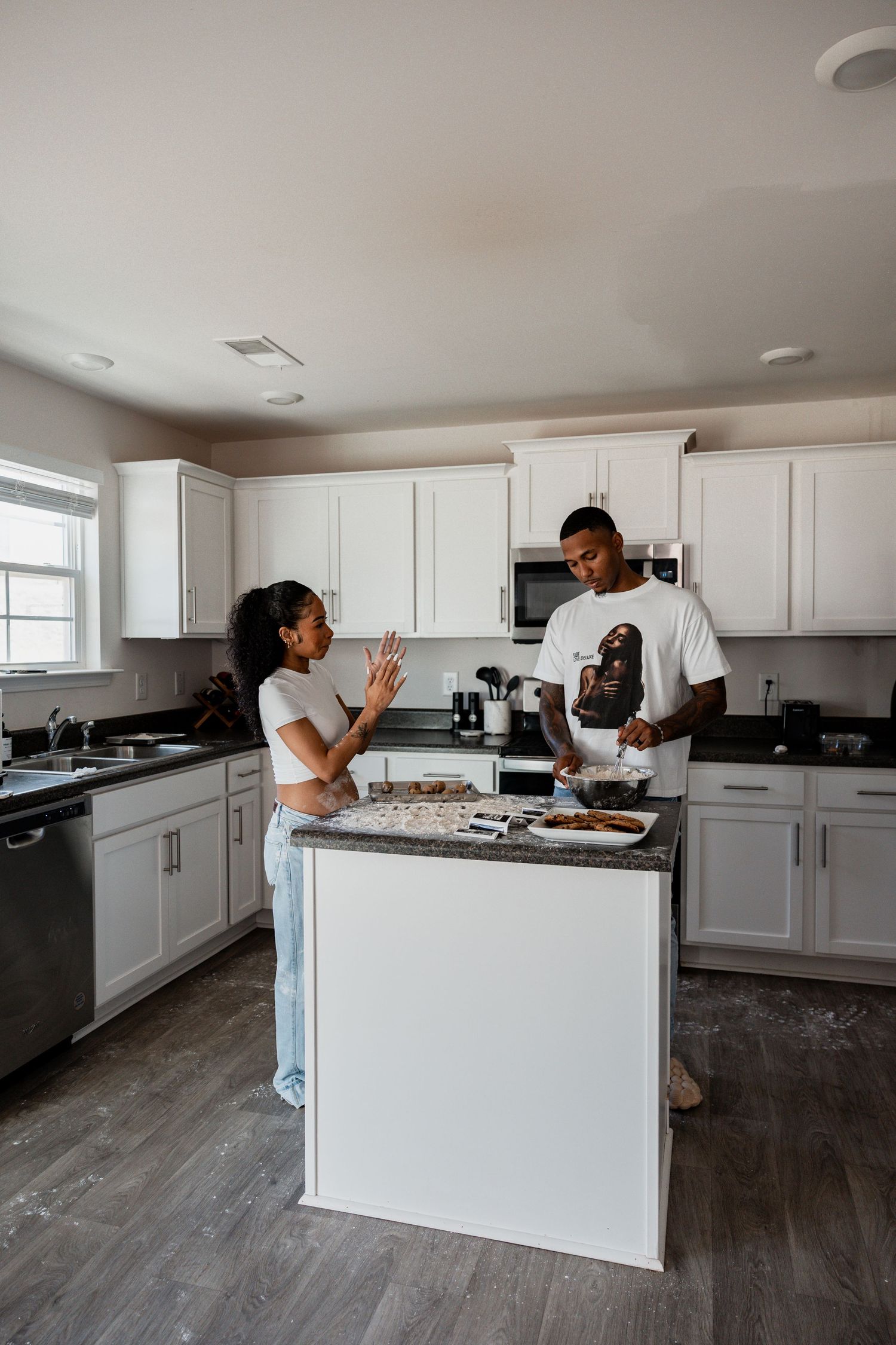 Young Black couple cooking together in a modern white kitchen with dark countertops.