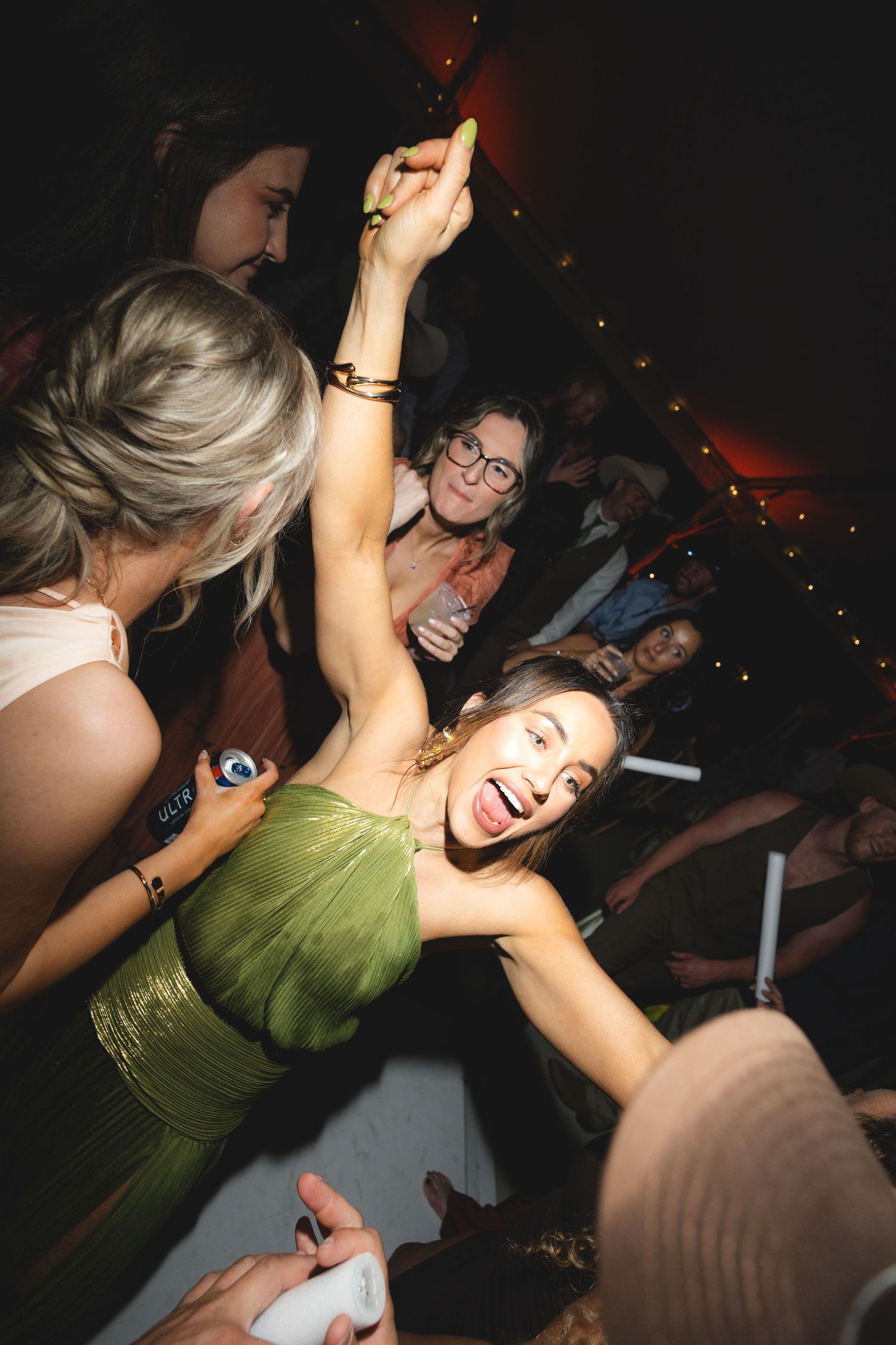Joyful wedding guest in green dress dancing with arm raised among a crowd at a lively wedding reception.