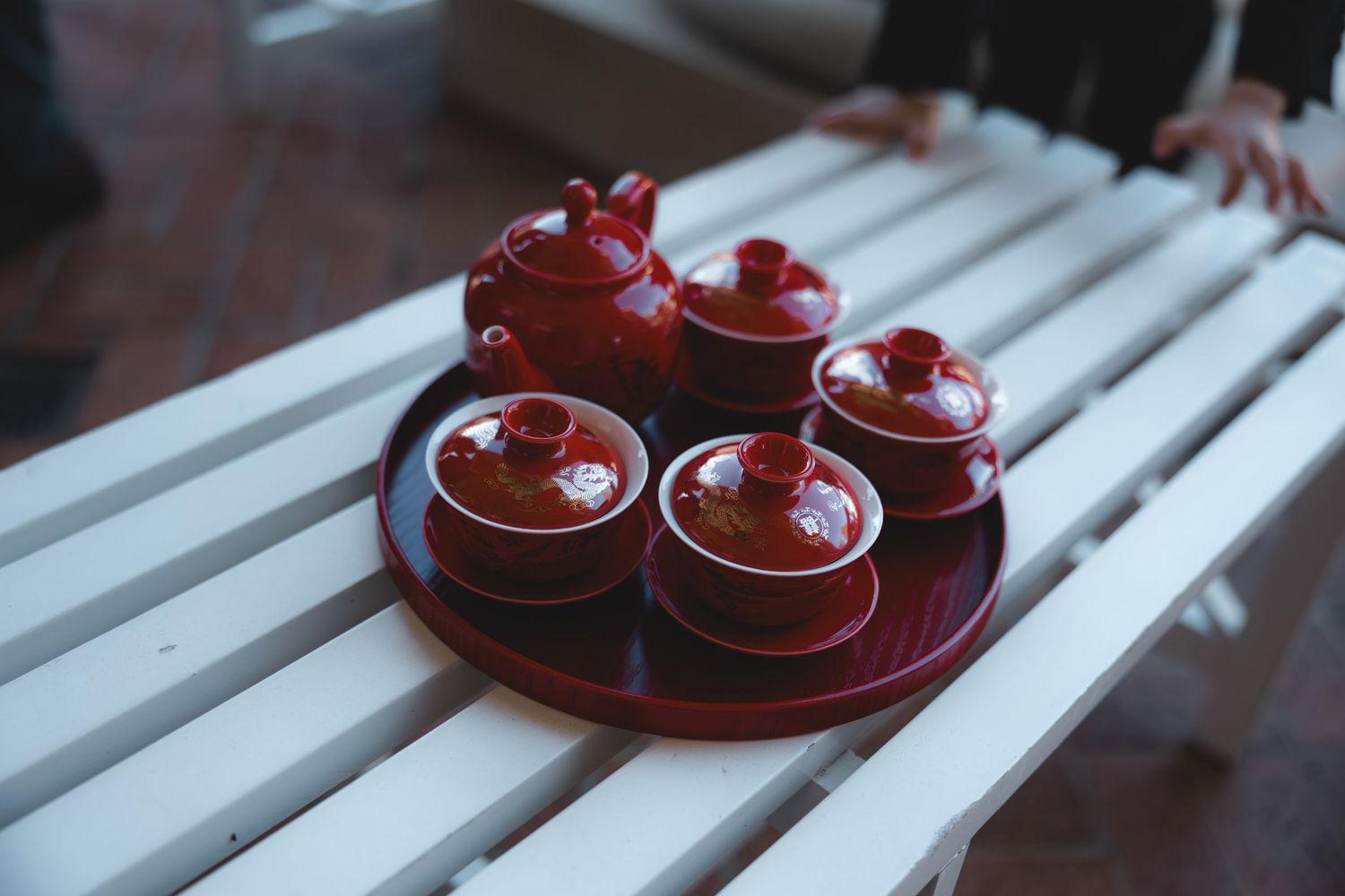 Traditional red Chinese tea set with teapot and covered cups arranged on a round tray on white bench.