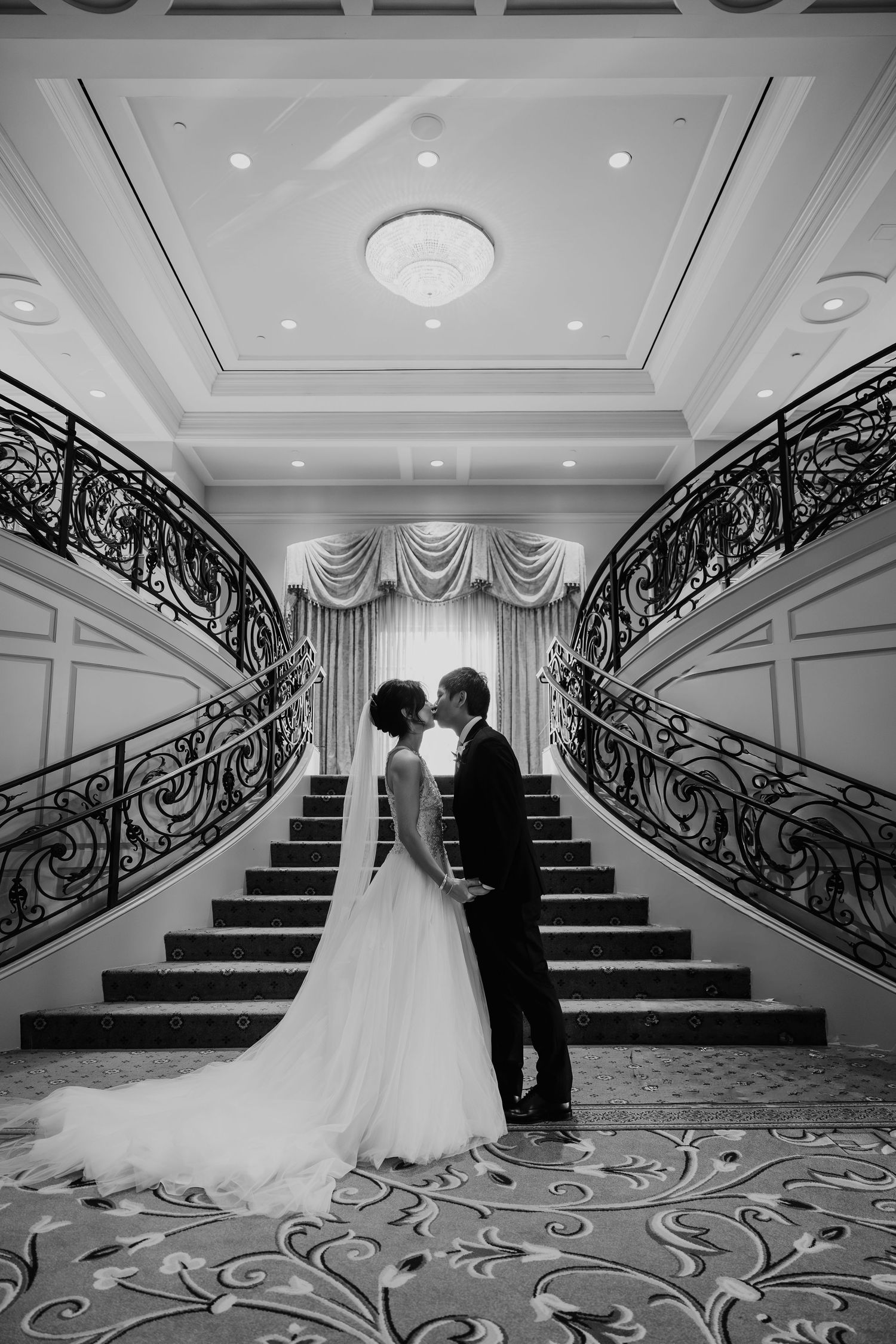 Black and white portrait of bride and groom sharing romantic moment at grand staircase.