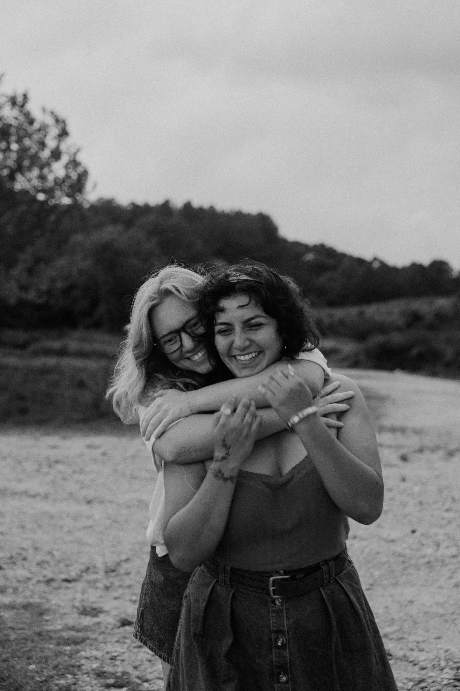 Two women sharing a warm embrace outdoors, smiling joyfully in a black and white photo.