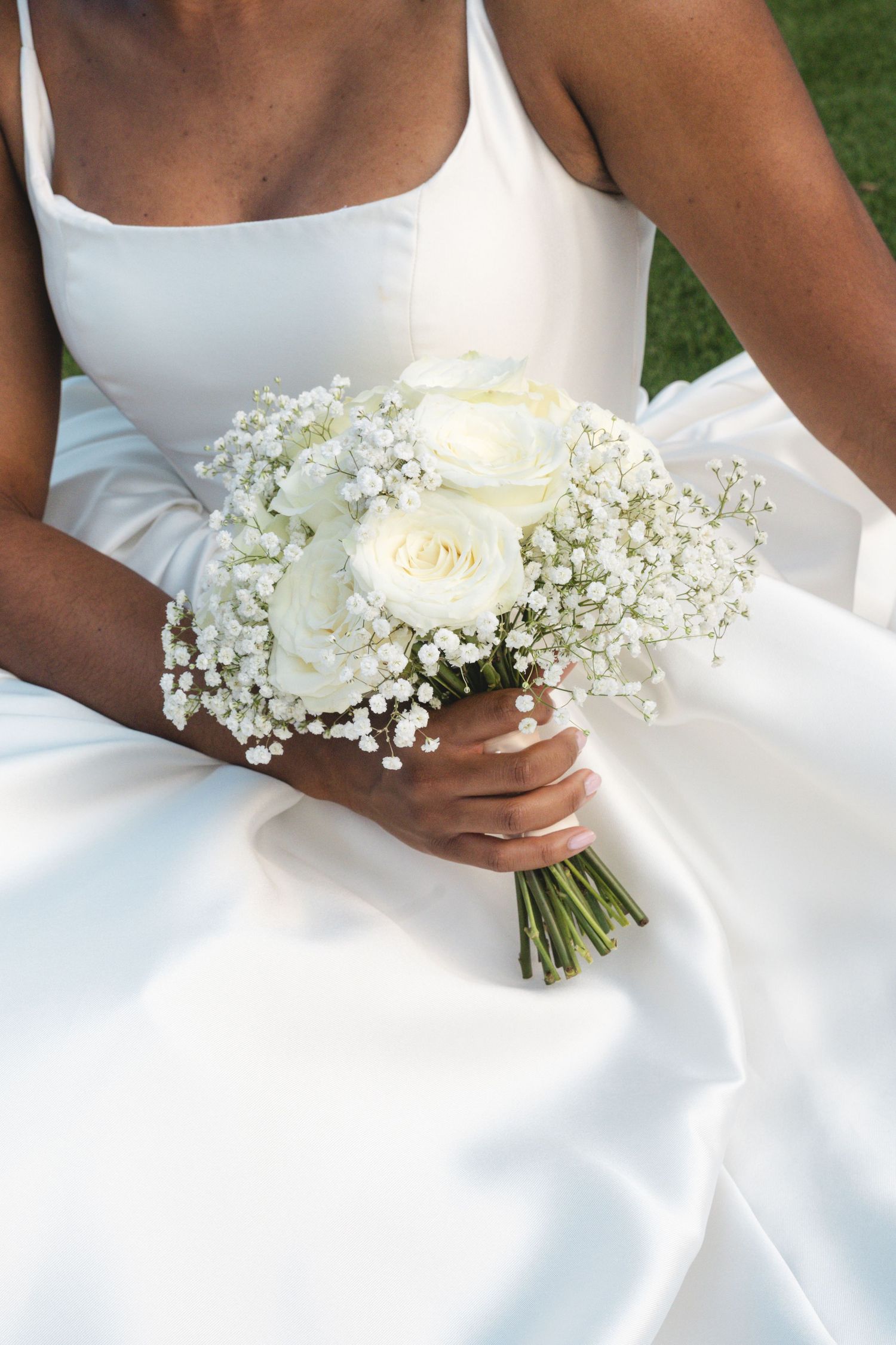 Bride in white satin gown holding elegant bouquet of white roses and baby's breath on her wedding day.