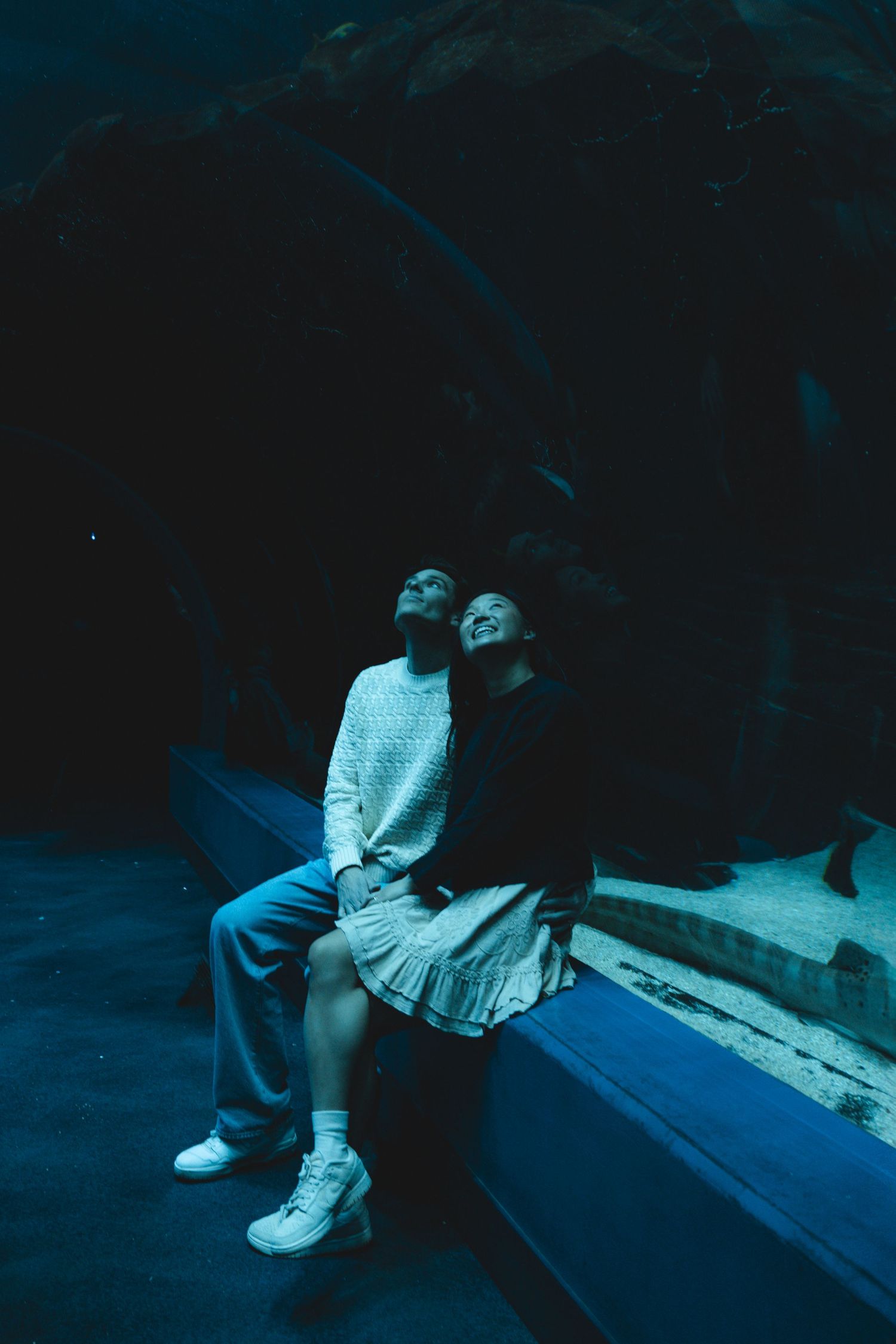 Two people sitting close together on a blue bench in dark moody lighting.