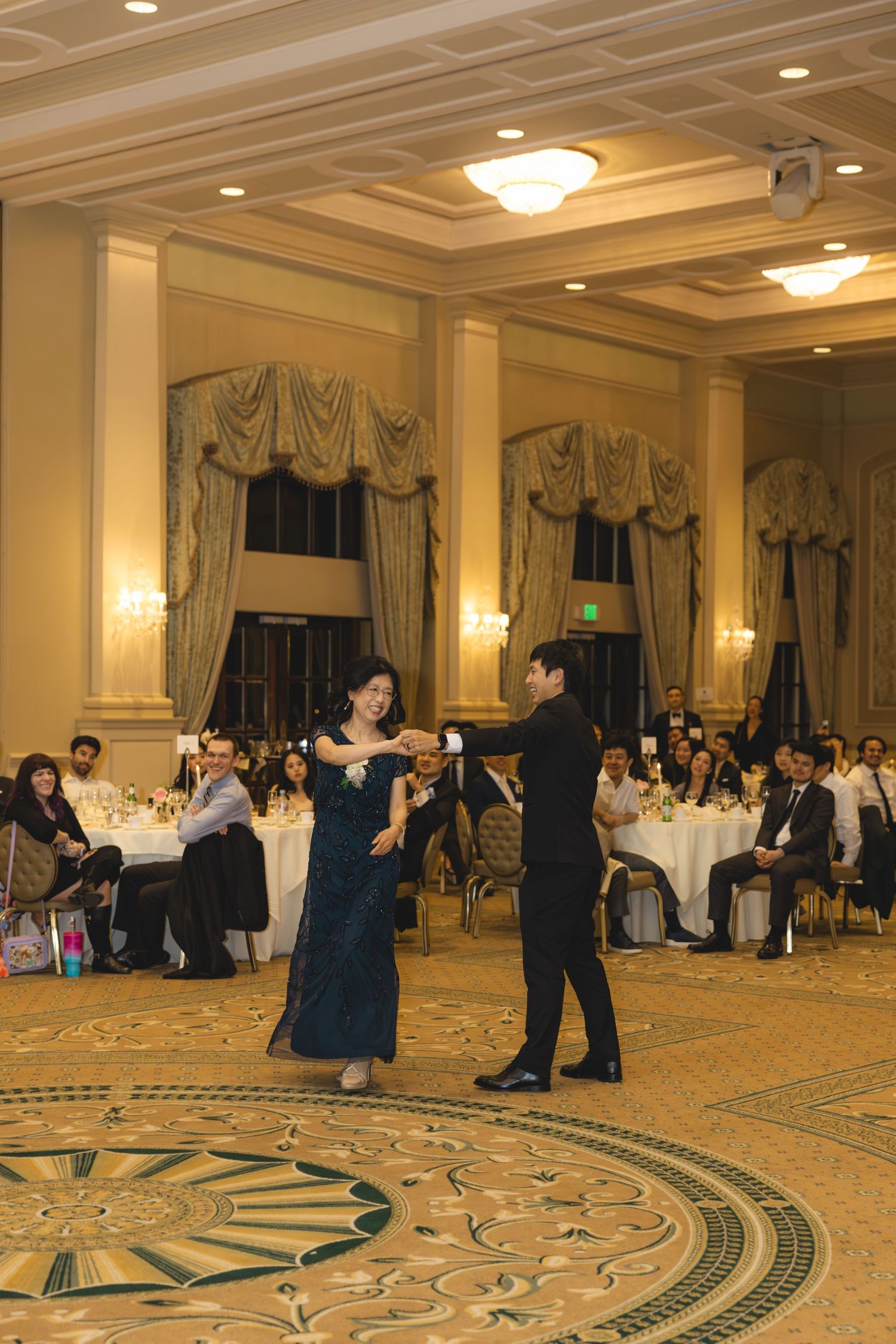 Groom dancing with mother in elegant ballroom during wedding reception parent dance.