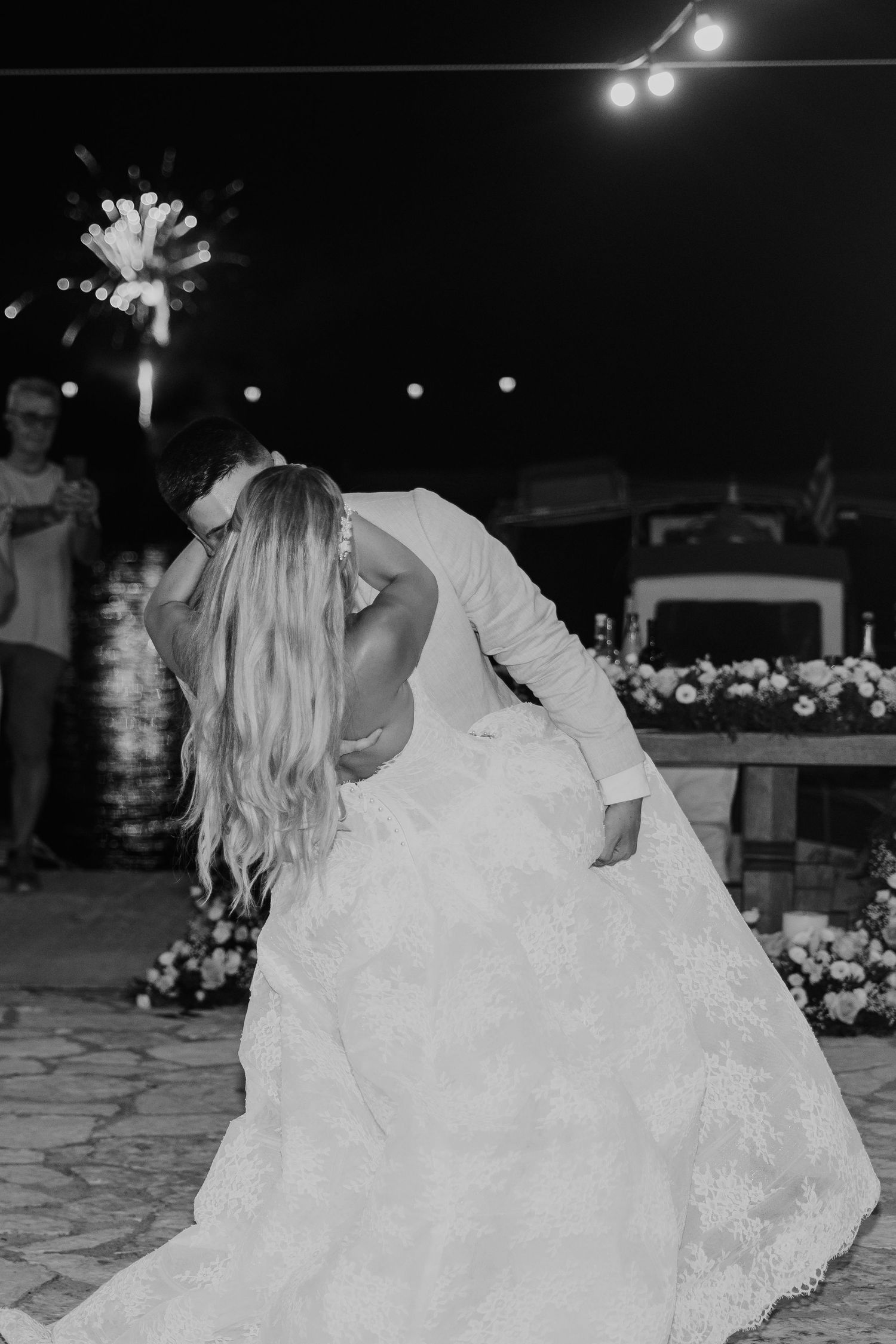Black and white photo of bride and groom sharing a romantic dip kiss at outdoor wedding reception with sparklers.