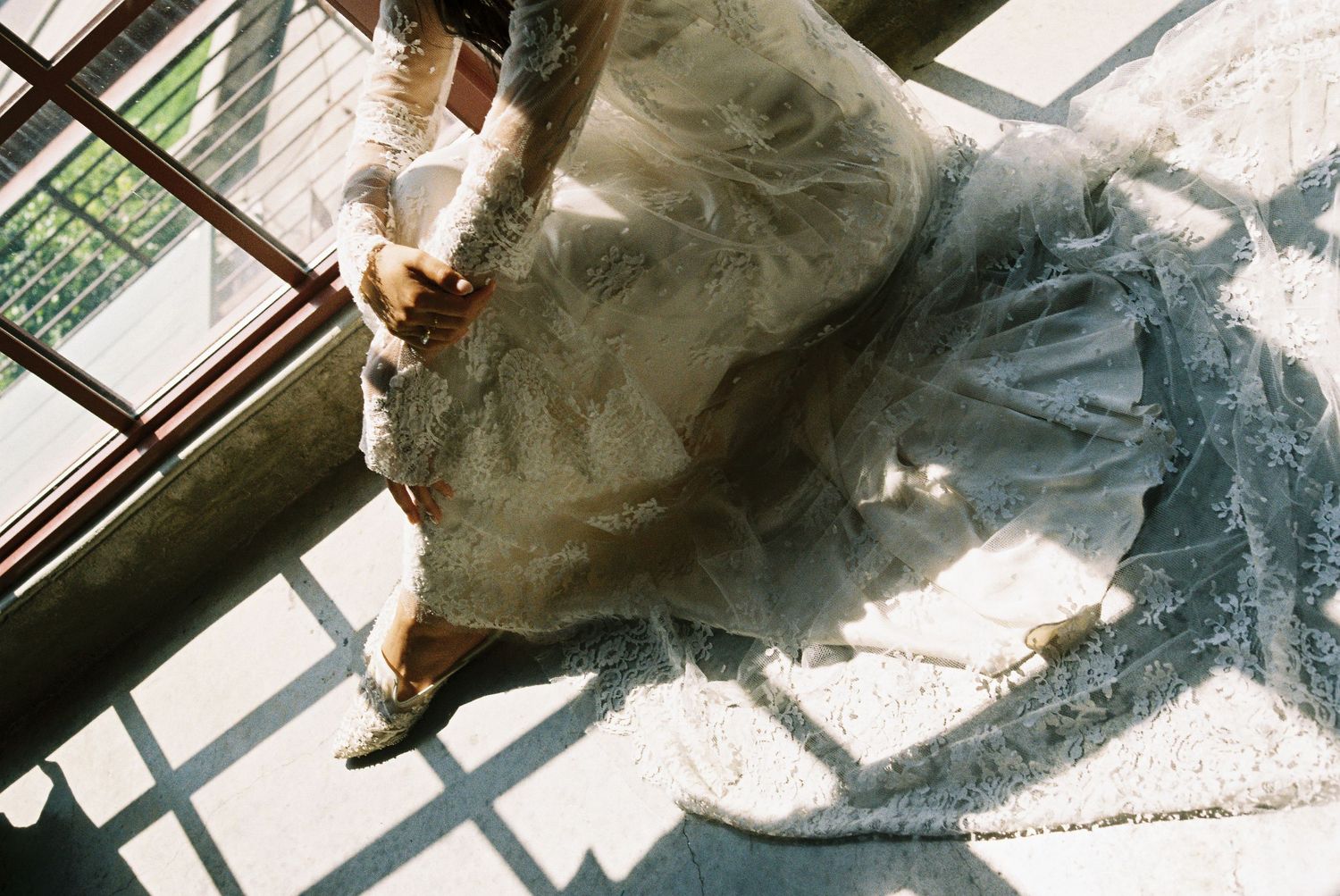 Aerial view of a bride in a flowing white lace wedding gown standing on a staircase in natural light.