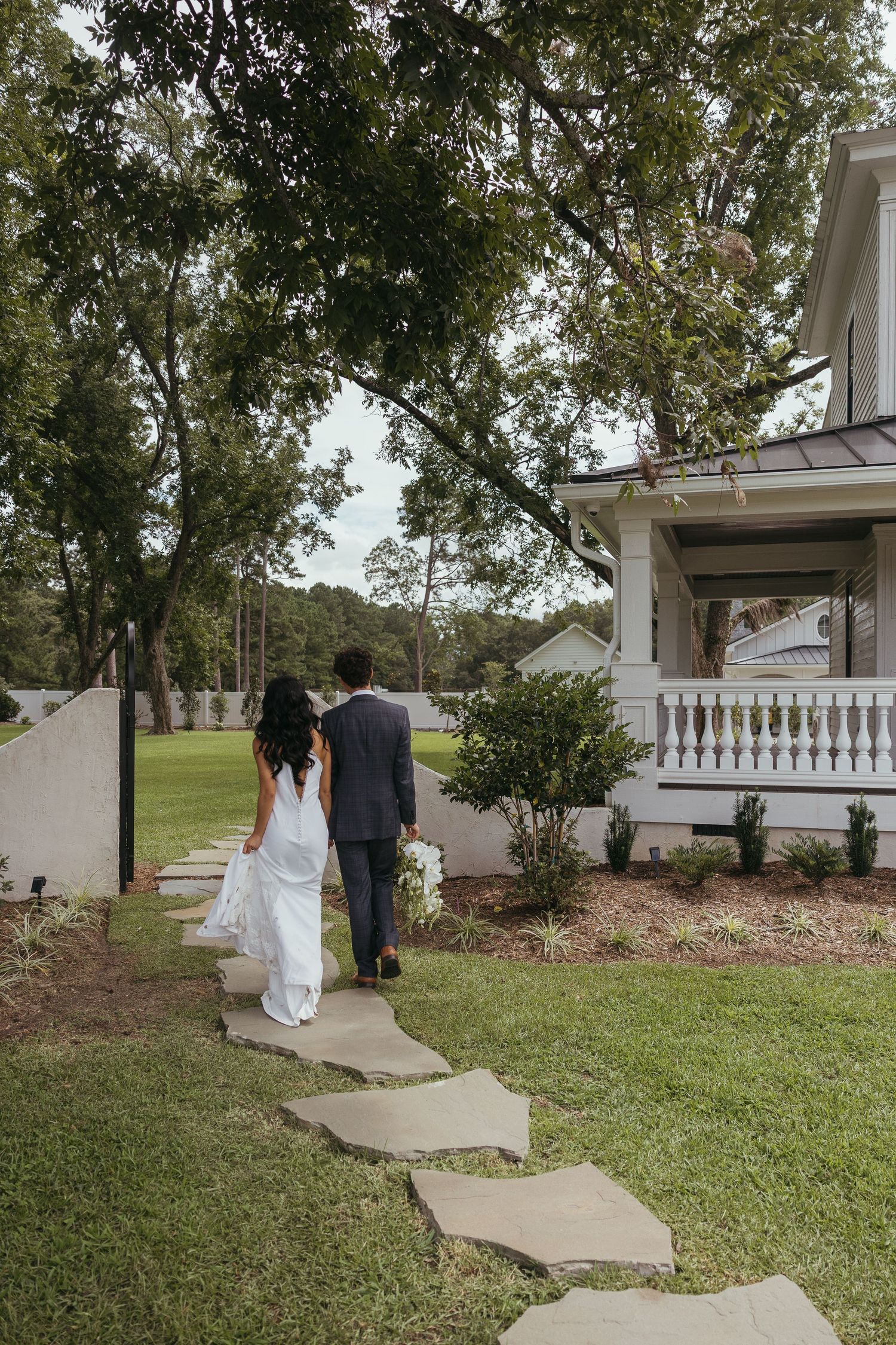 A couple walks up a curved concrete path leading to a white building entrance on a grassy lawn.