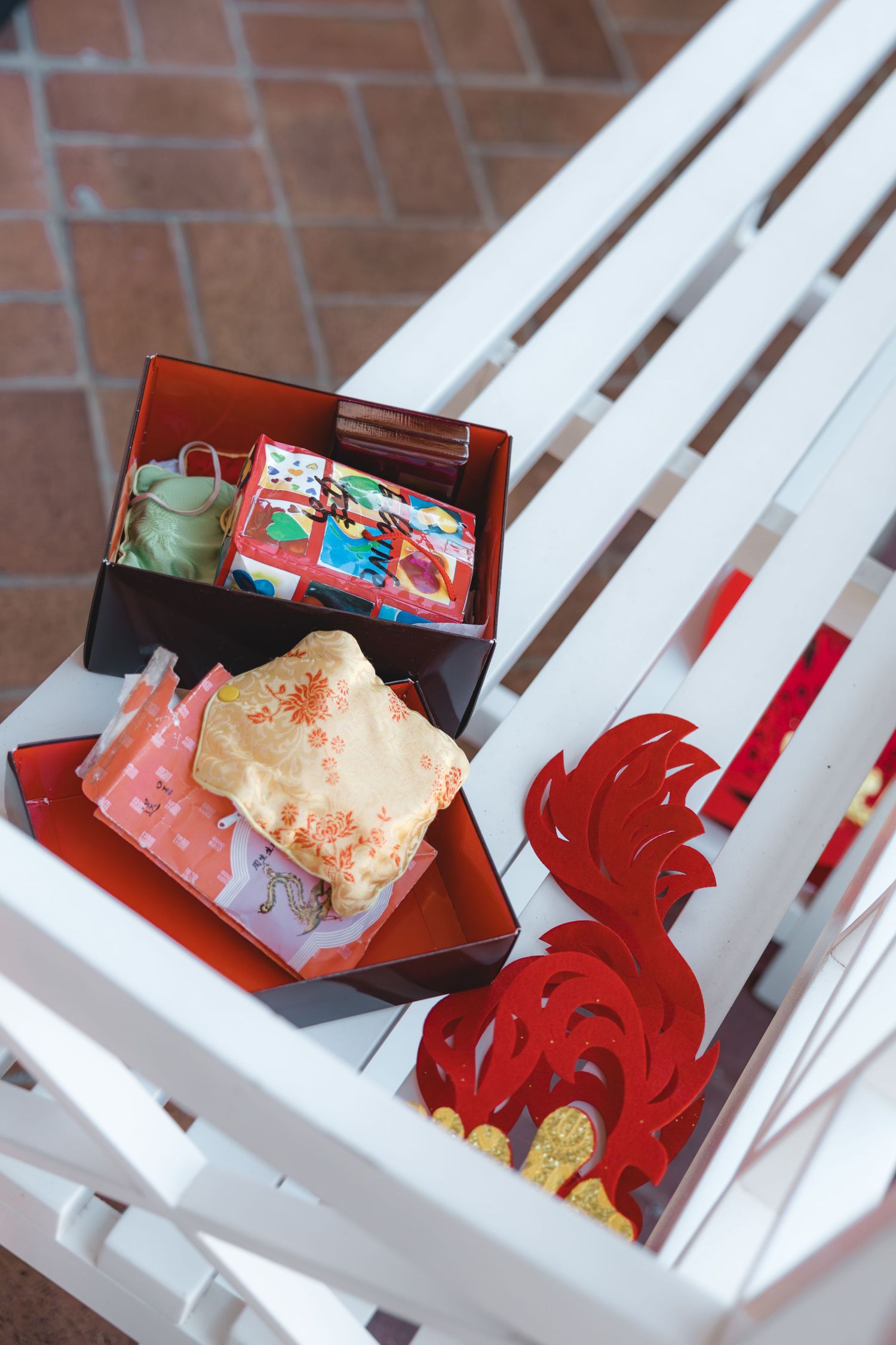 Traditional Chinese wedding gift boxes with red decorations on a white bench.