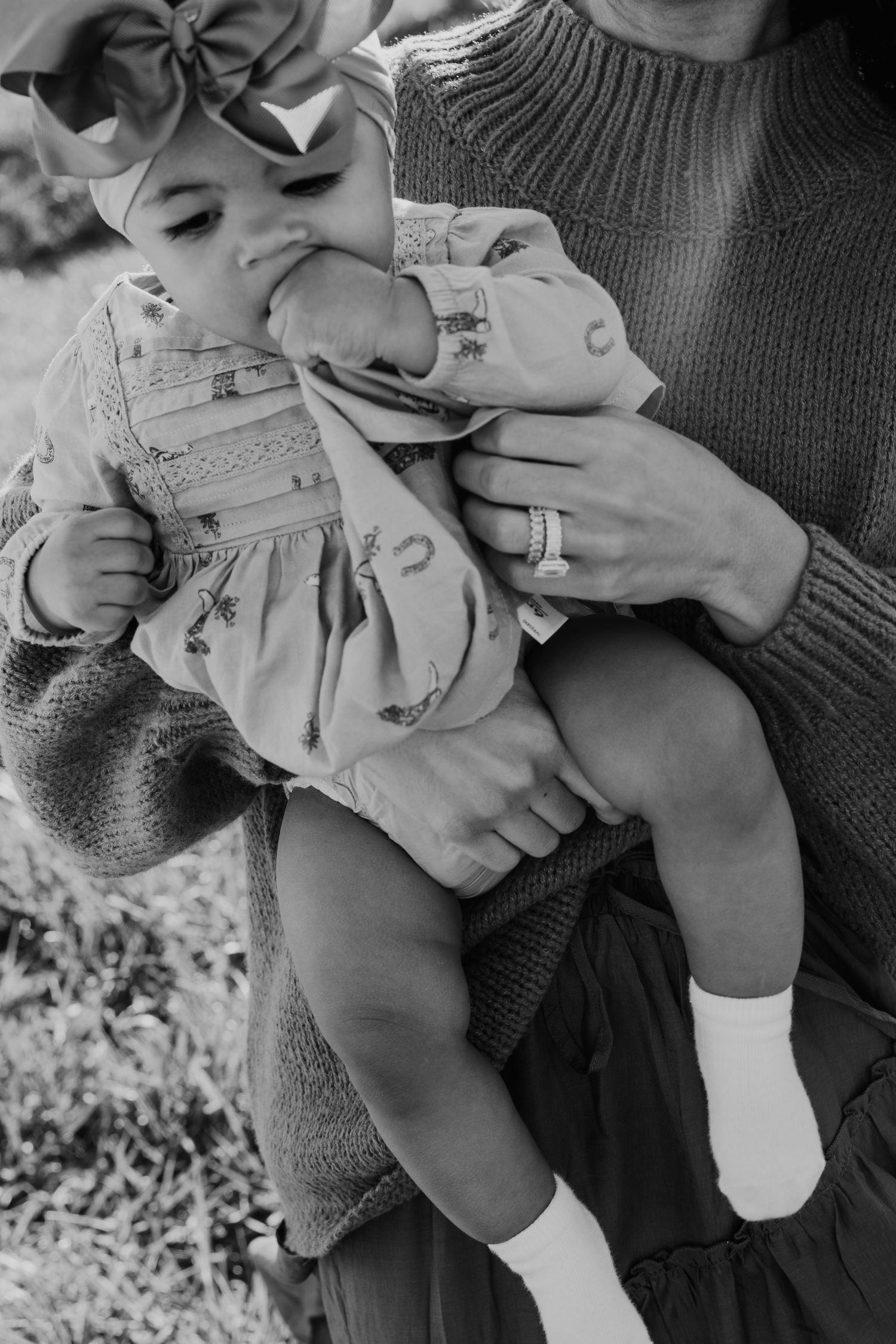 Black and white photo of a mother holding her baby girl wearing a bow headband and floral dress.