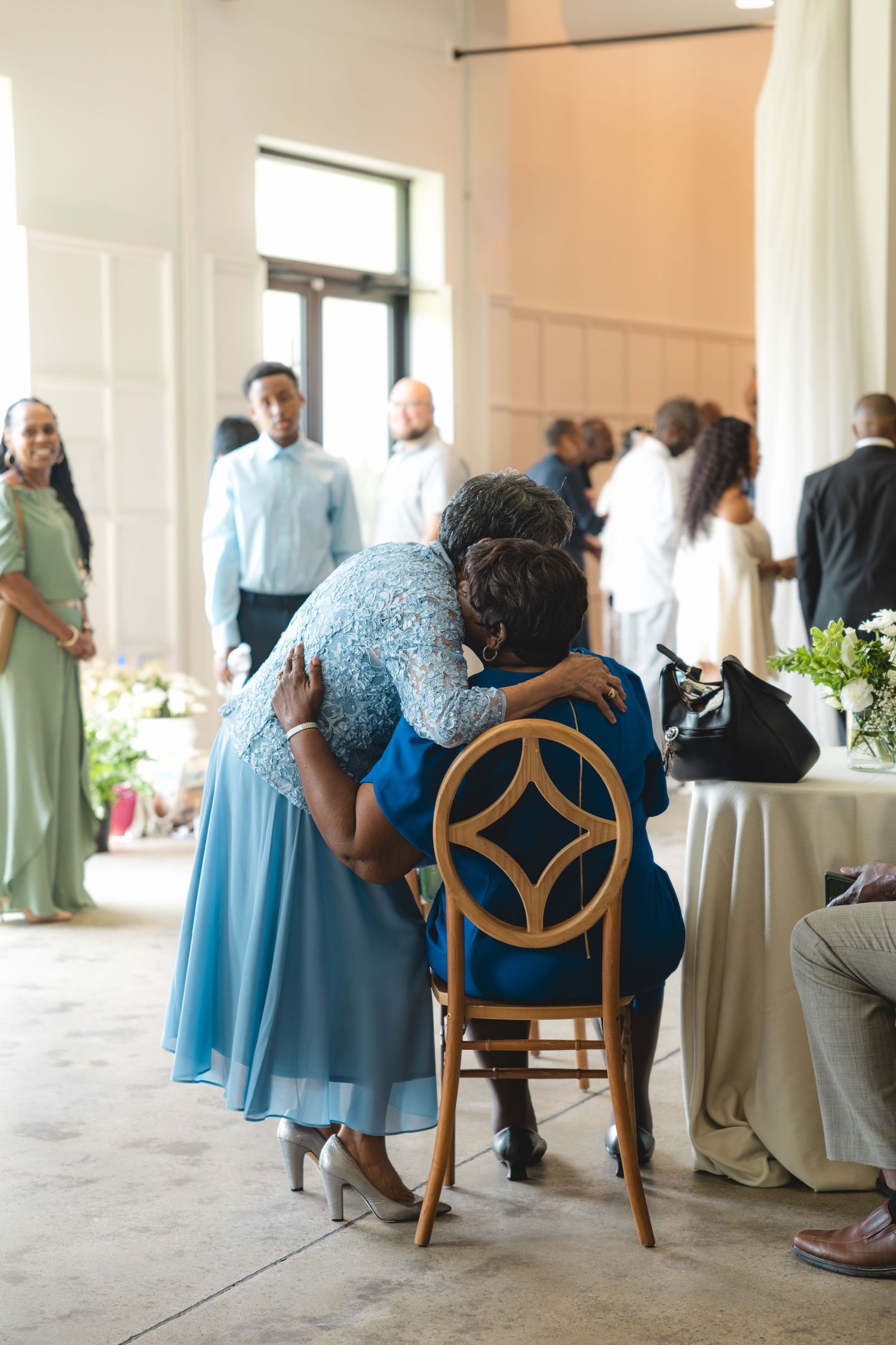 Two women in blue dresses share a warm embrace at an elegant wedding reception venue.