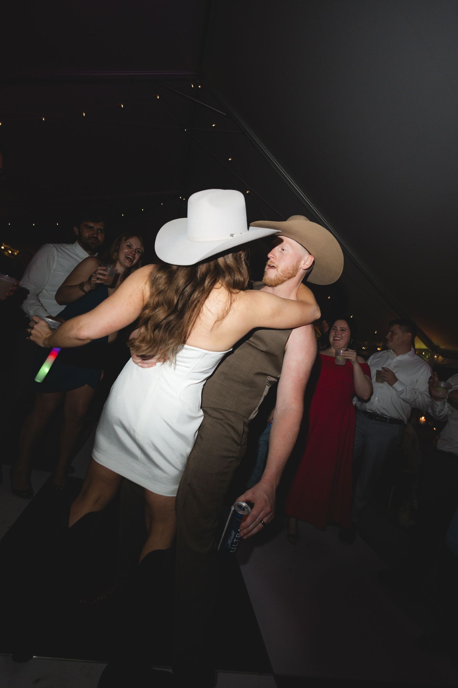 Couple in cowboy hats sharing a close dance embrace on the dance floor at a lively wedding reception.