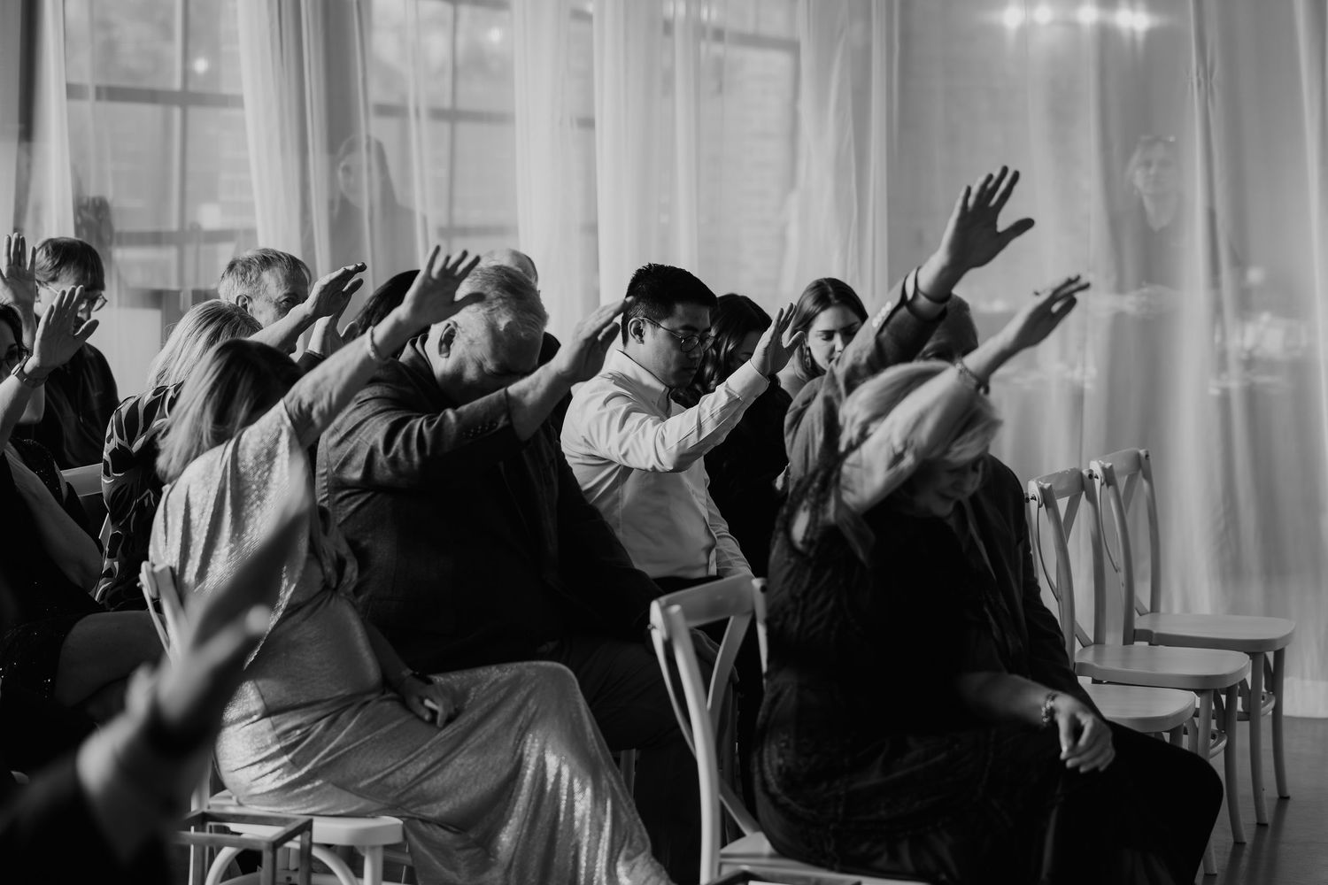 Black and white photo of wedding guests raising their hands during an emotional ceremony blessing.