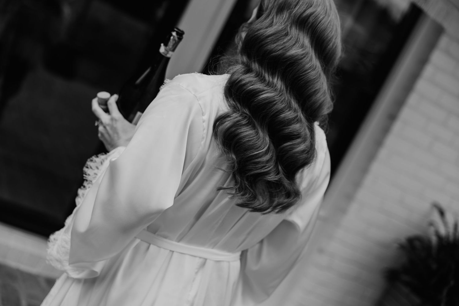 Black and white photo of bride with elegant updo hairstyle wearing a white bridal robe.