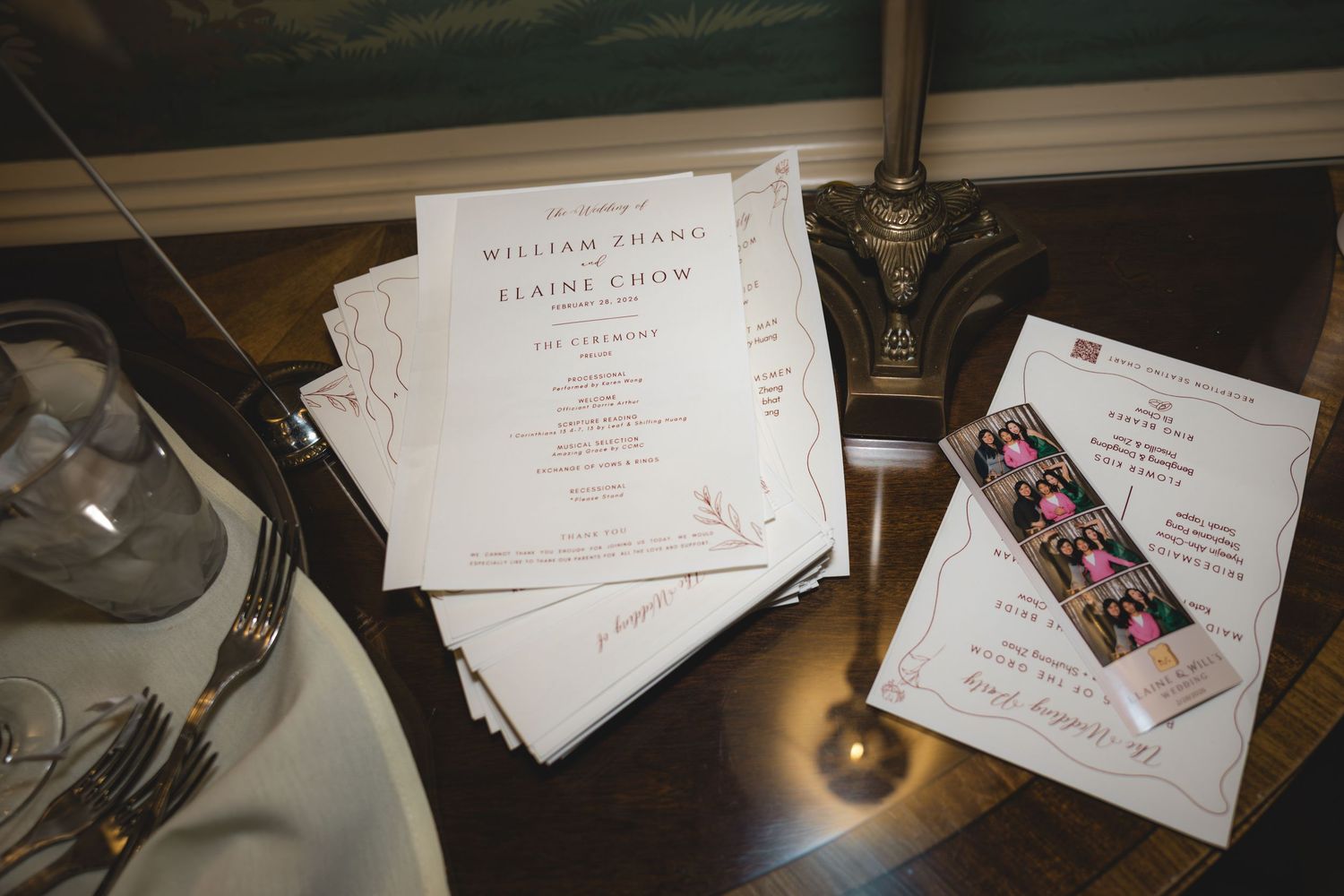 Wedding invitations and programs for William Thang and Elaine Chow displayed on a wooden table with photo booth strip.