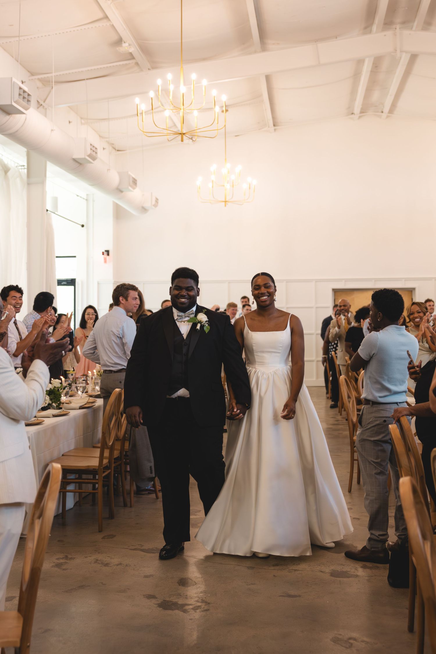 Newlyweds walk into reception hall as guests applaud their entrance.
