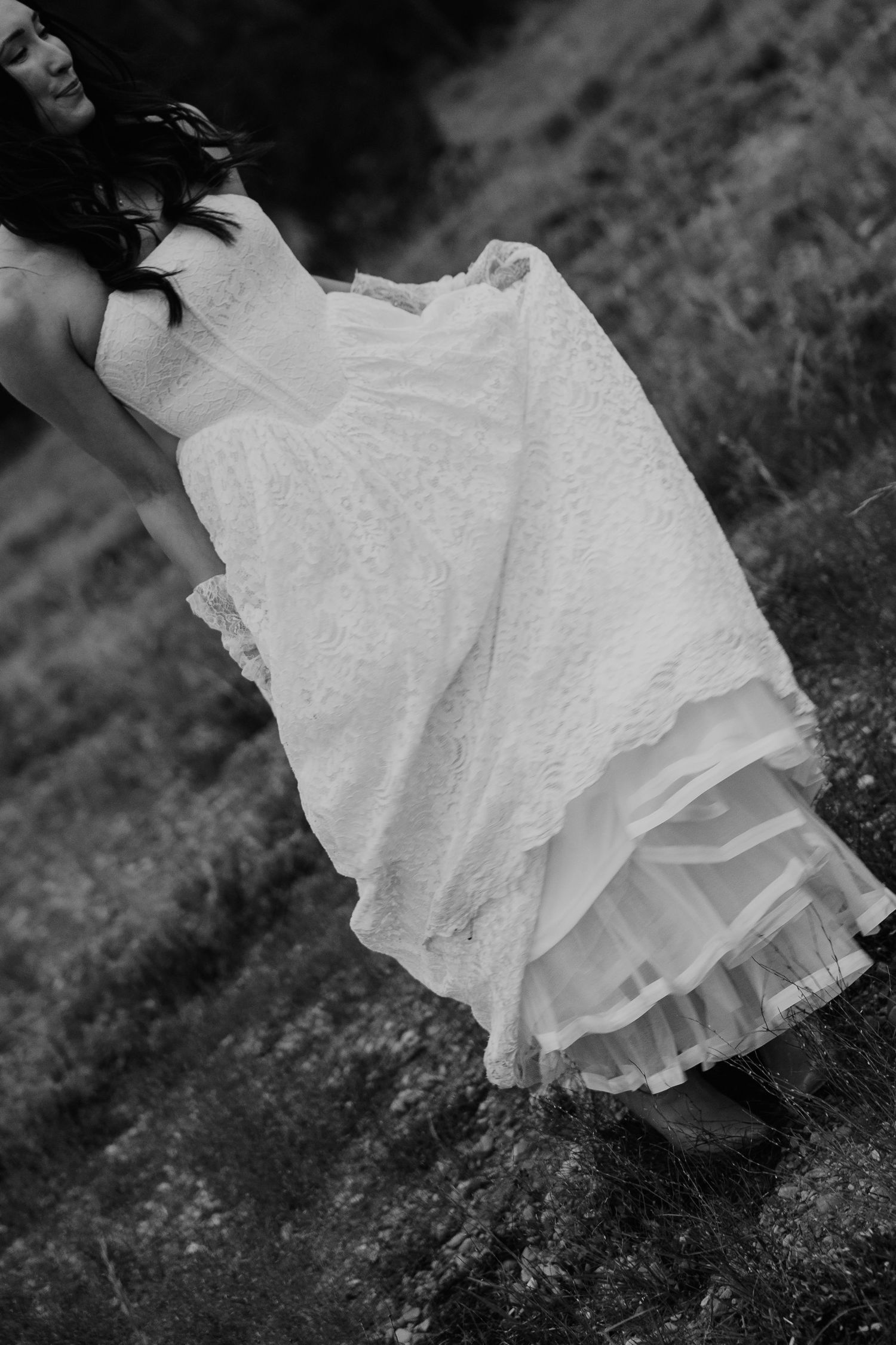Black and white photo of a bride in a lace wedding dress lifting her skirt outdoors.