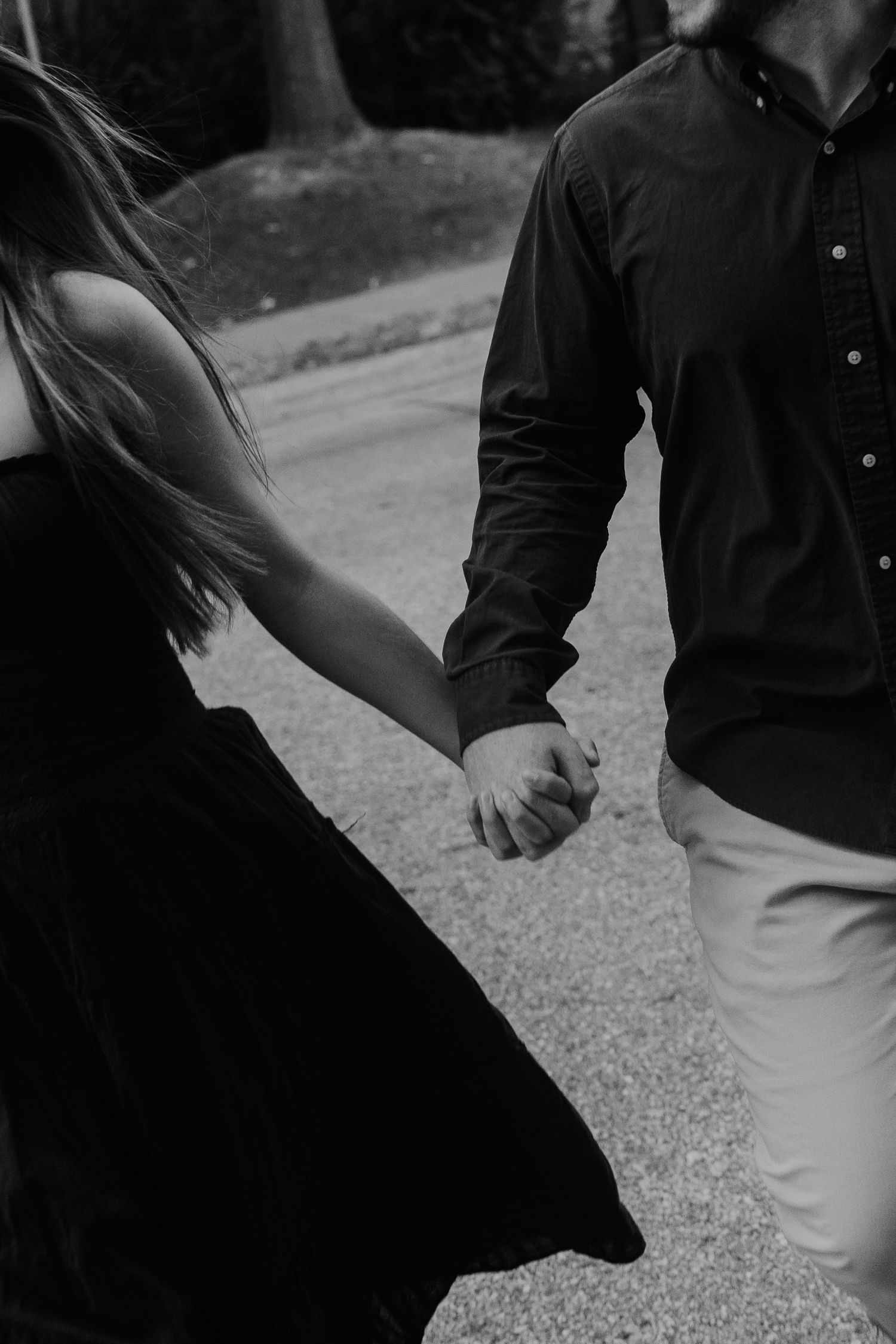 Black and white photo of a couple holding hands while walking, woman in flowing dress and man in dark shirt.