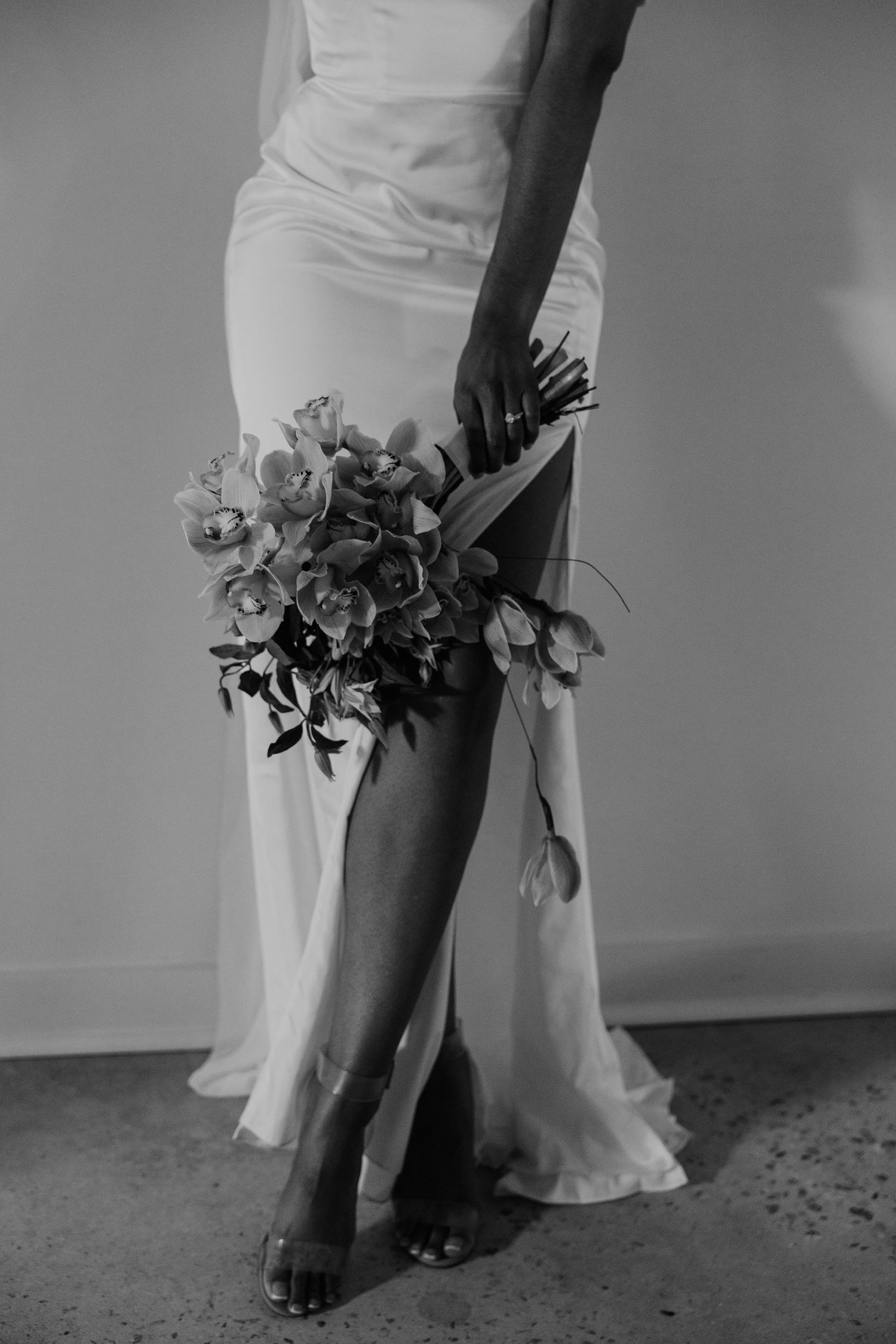 Black and white bridal photo featuring a slit gown, floral bouquet, and strappy heels.