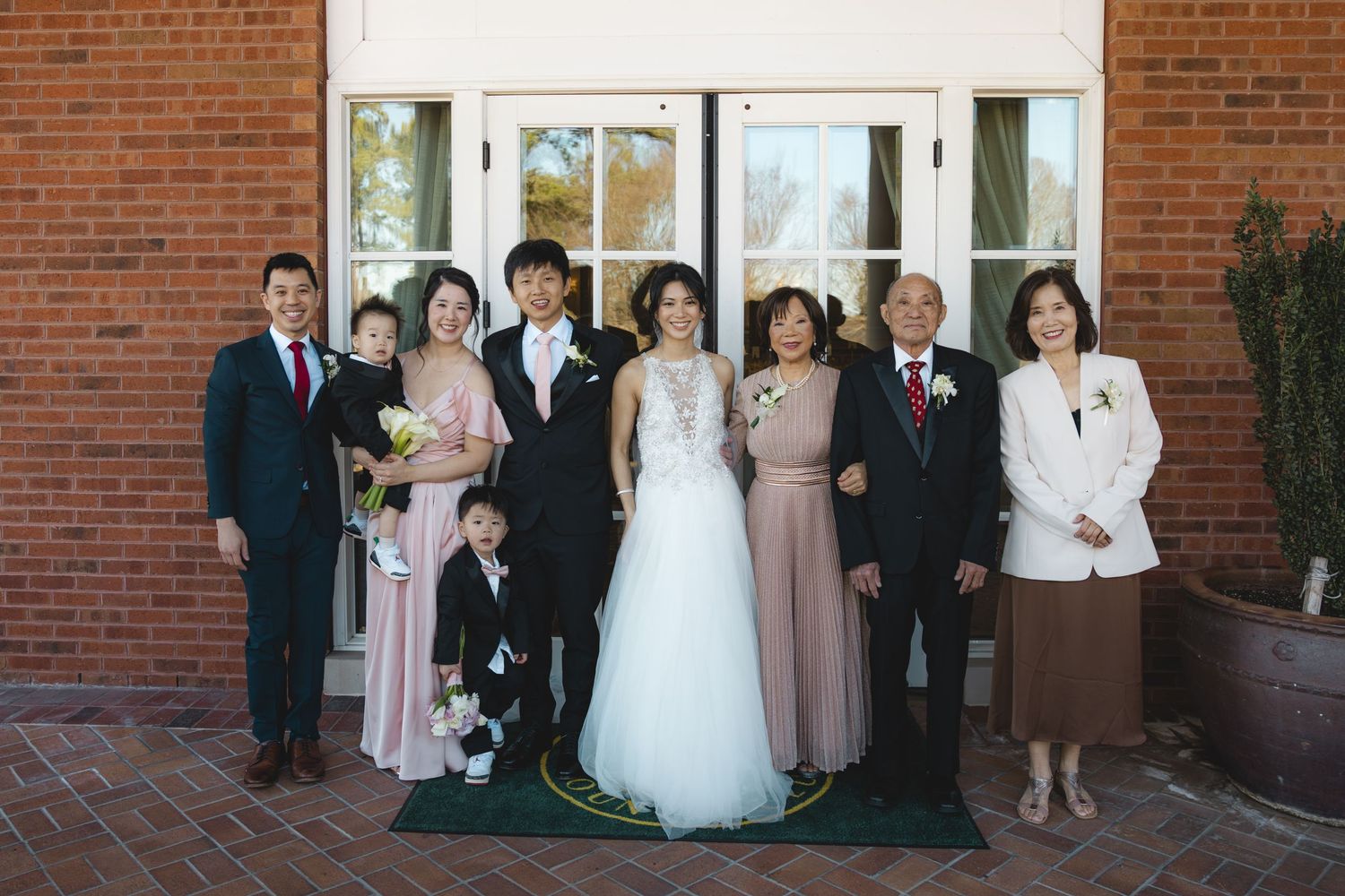 Wedding couple posing with family members in front of brick venue entrance.