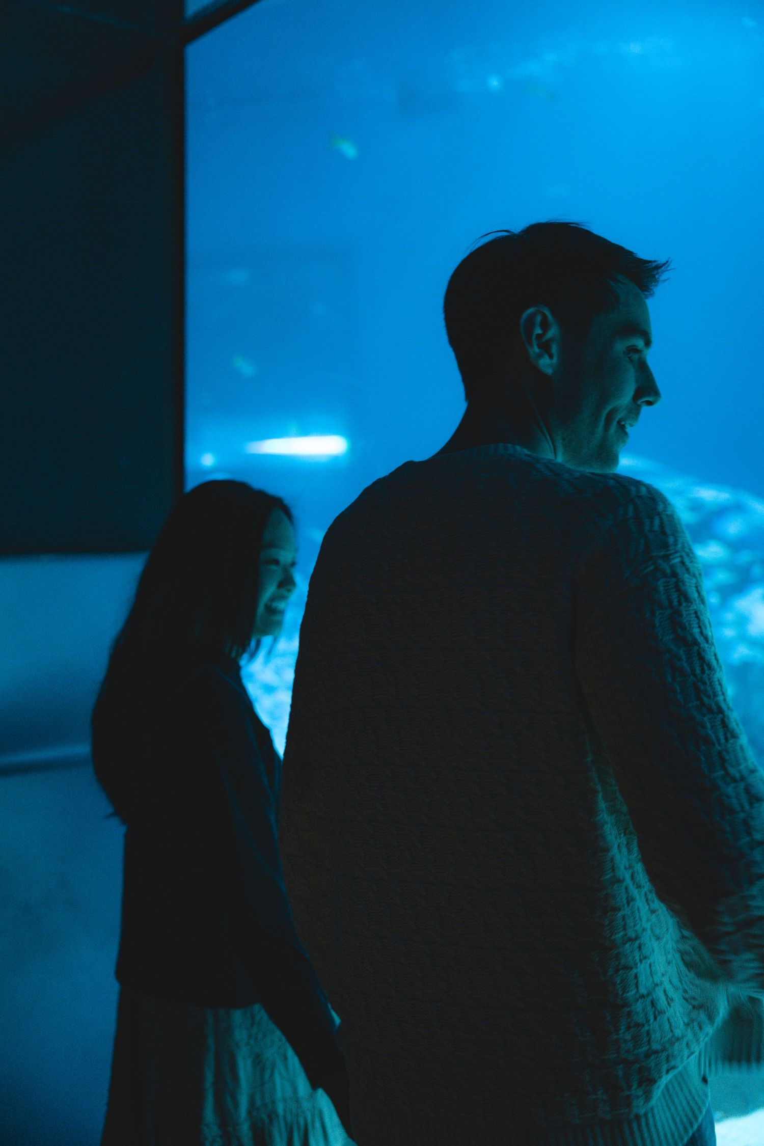 Silhouetted figures viewing an aquarium exhibit illuminated by blue lighting.