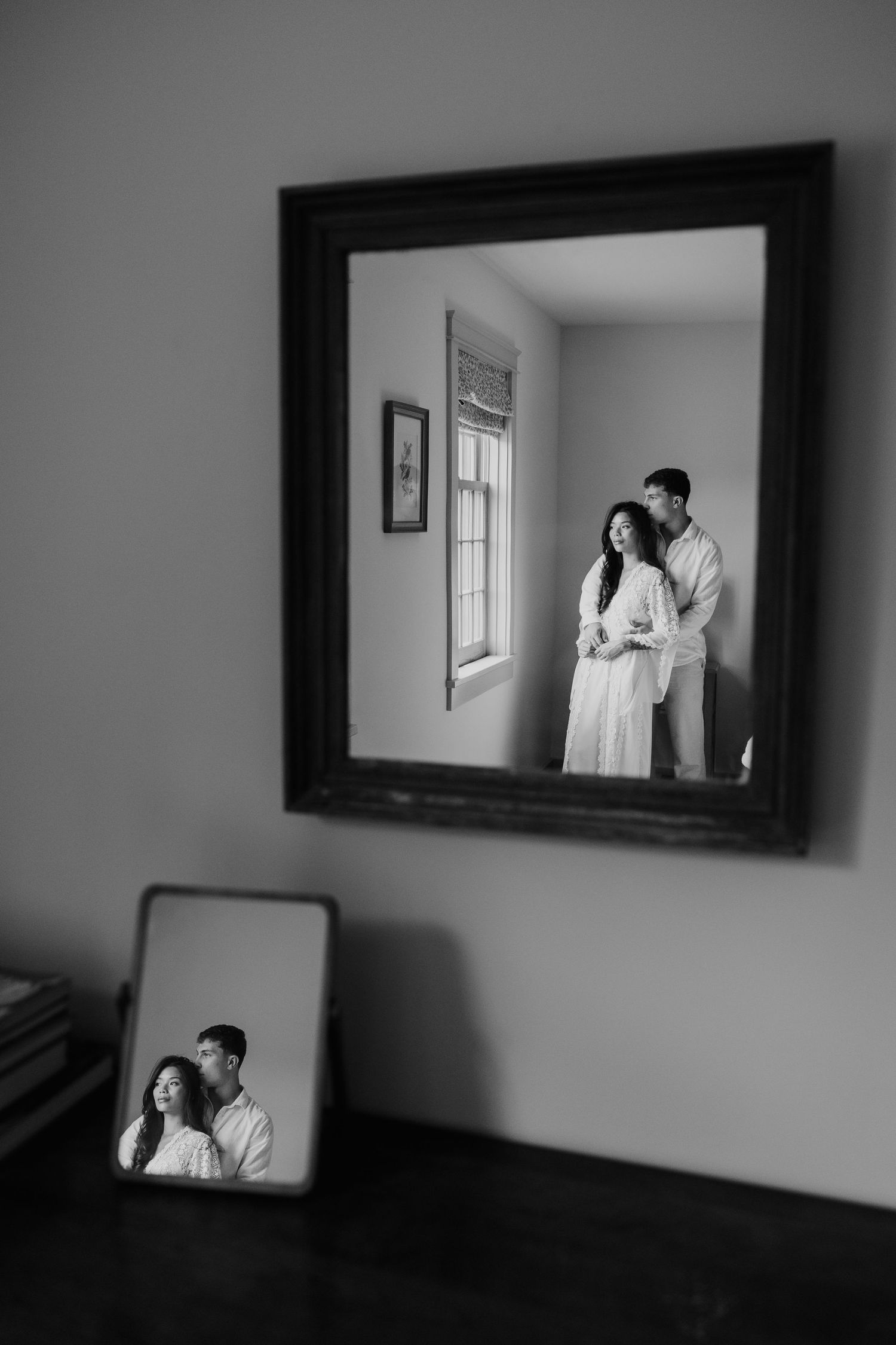 Black and white photo of a couple embracing, reflected in two mirrors on a wall and dresser.