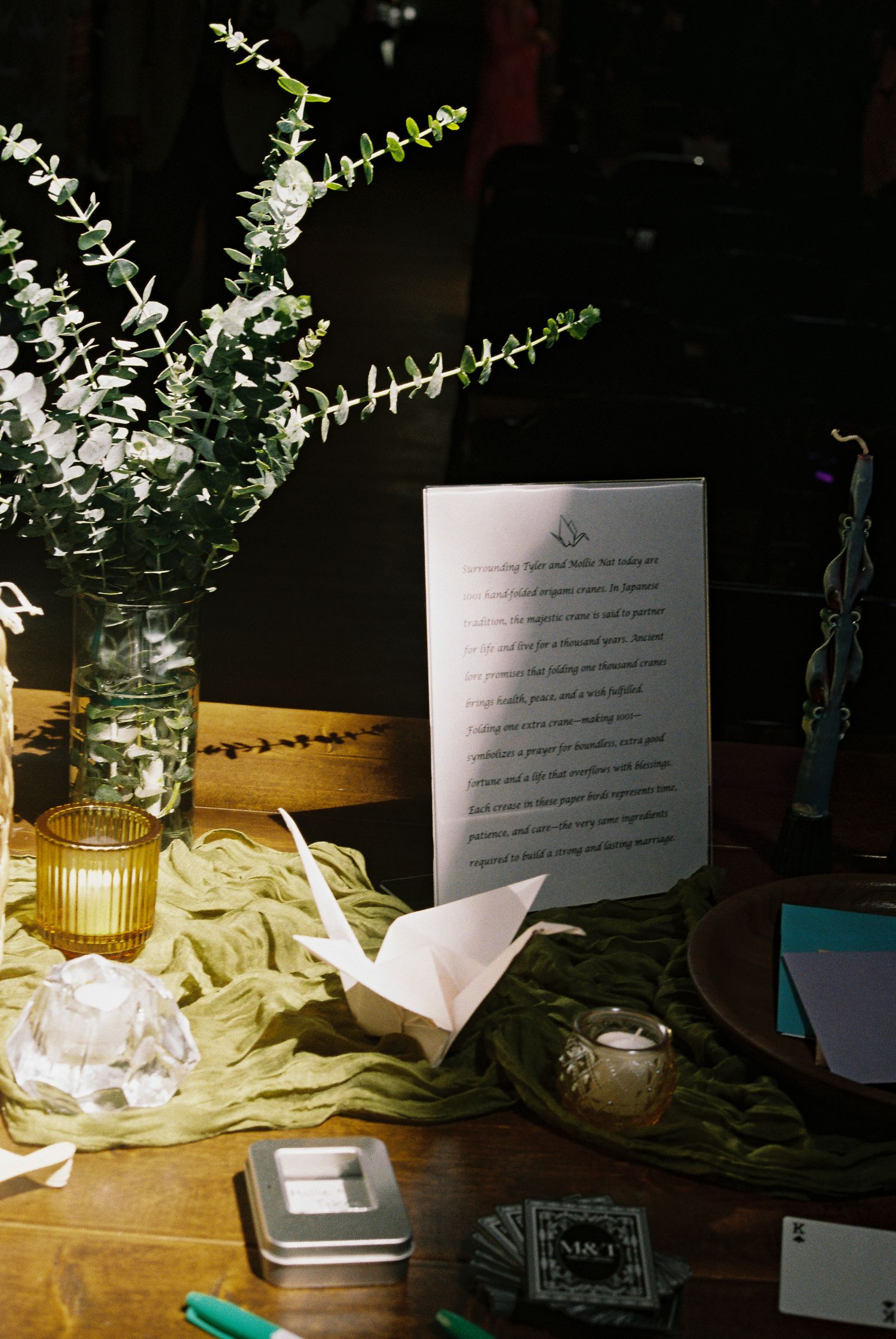 Elegant wedding table with origami crane, greenery, amber candle, and a framed poem on rustic wood.