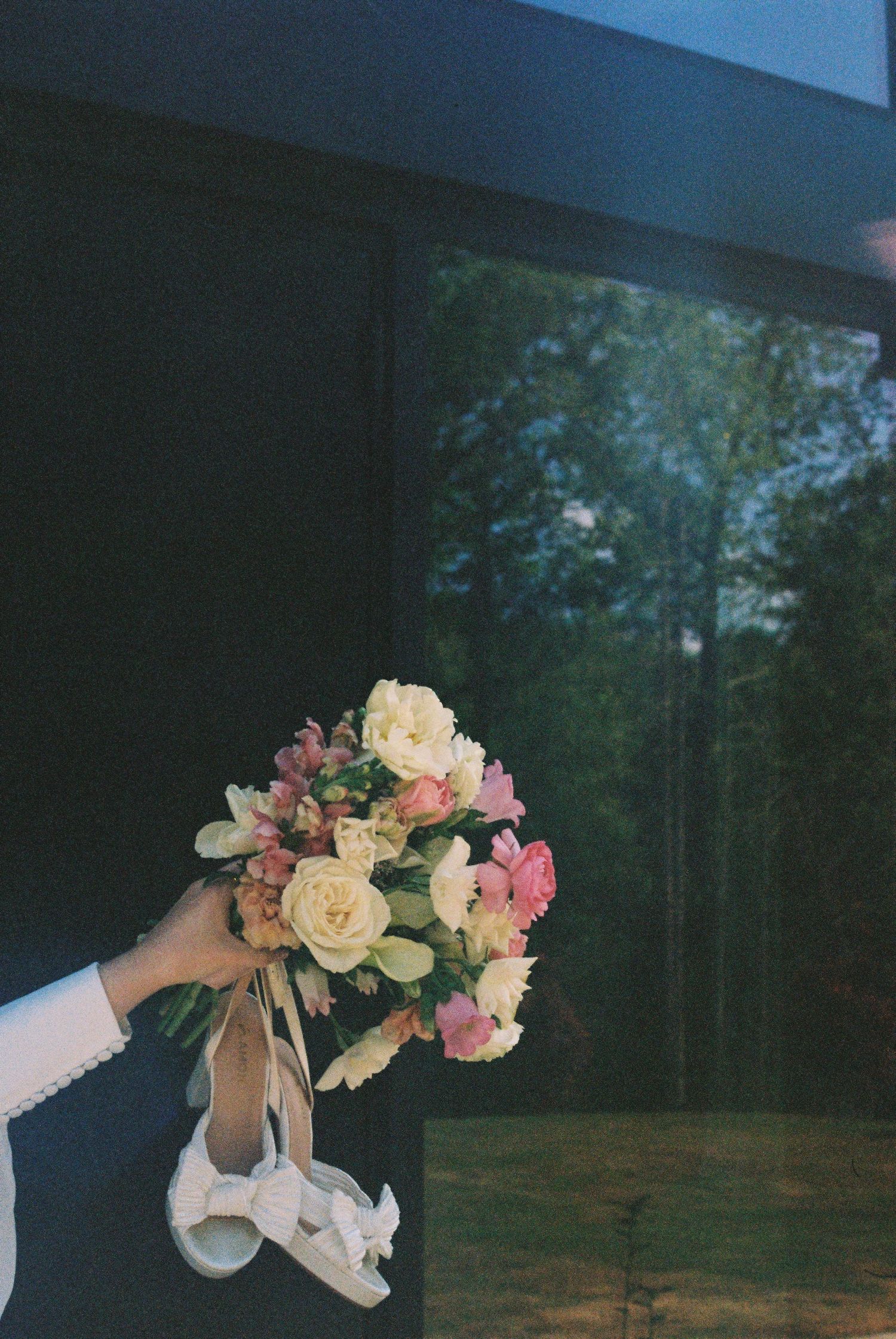 Hand holding a bridal bouquet of pink and white flowers with wedding heels at an elegant venue.