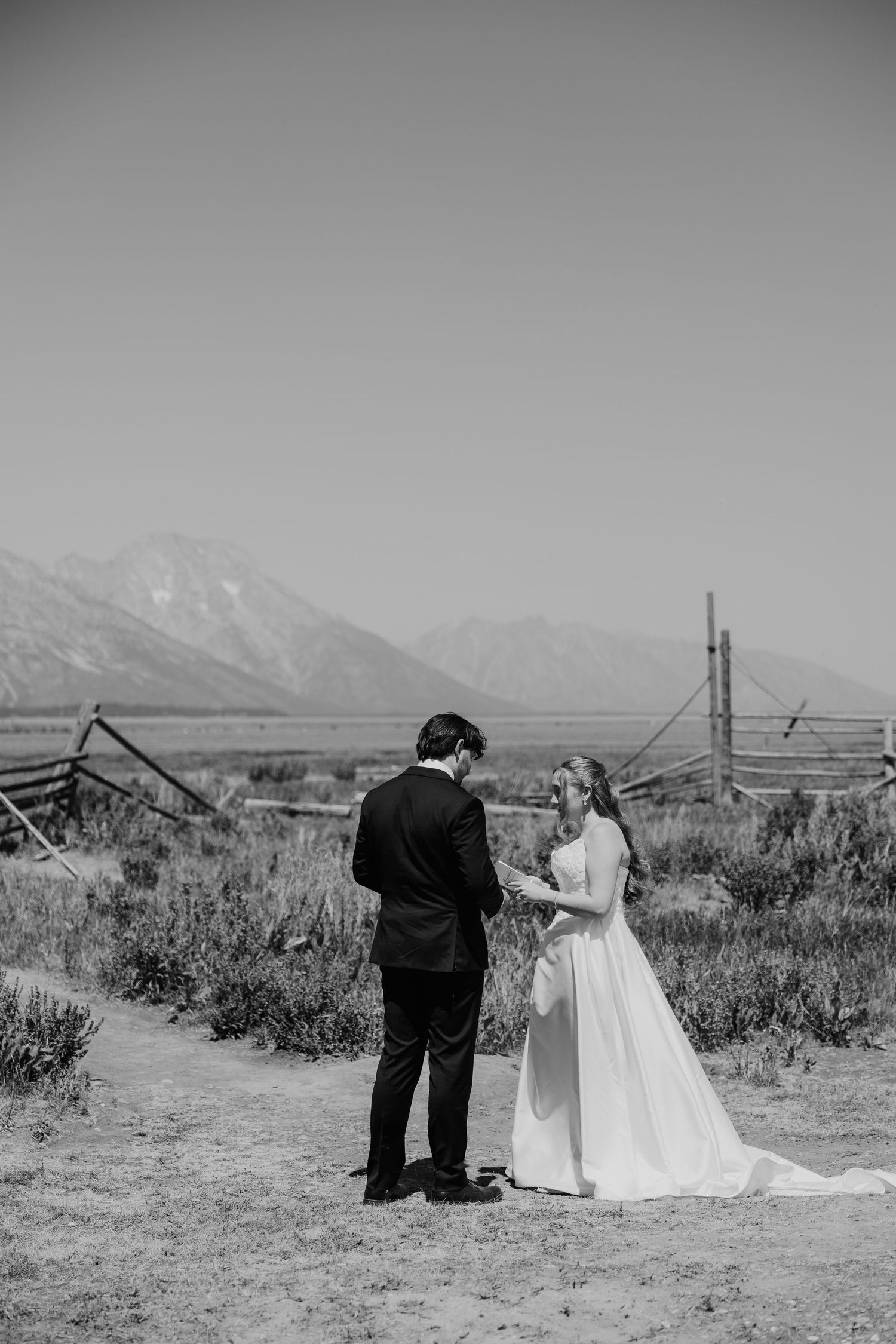 Black and white photo of a bride and groom exchanging vows outdoors with Grand Teton mountains in the background.