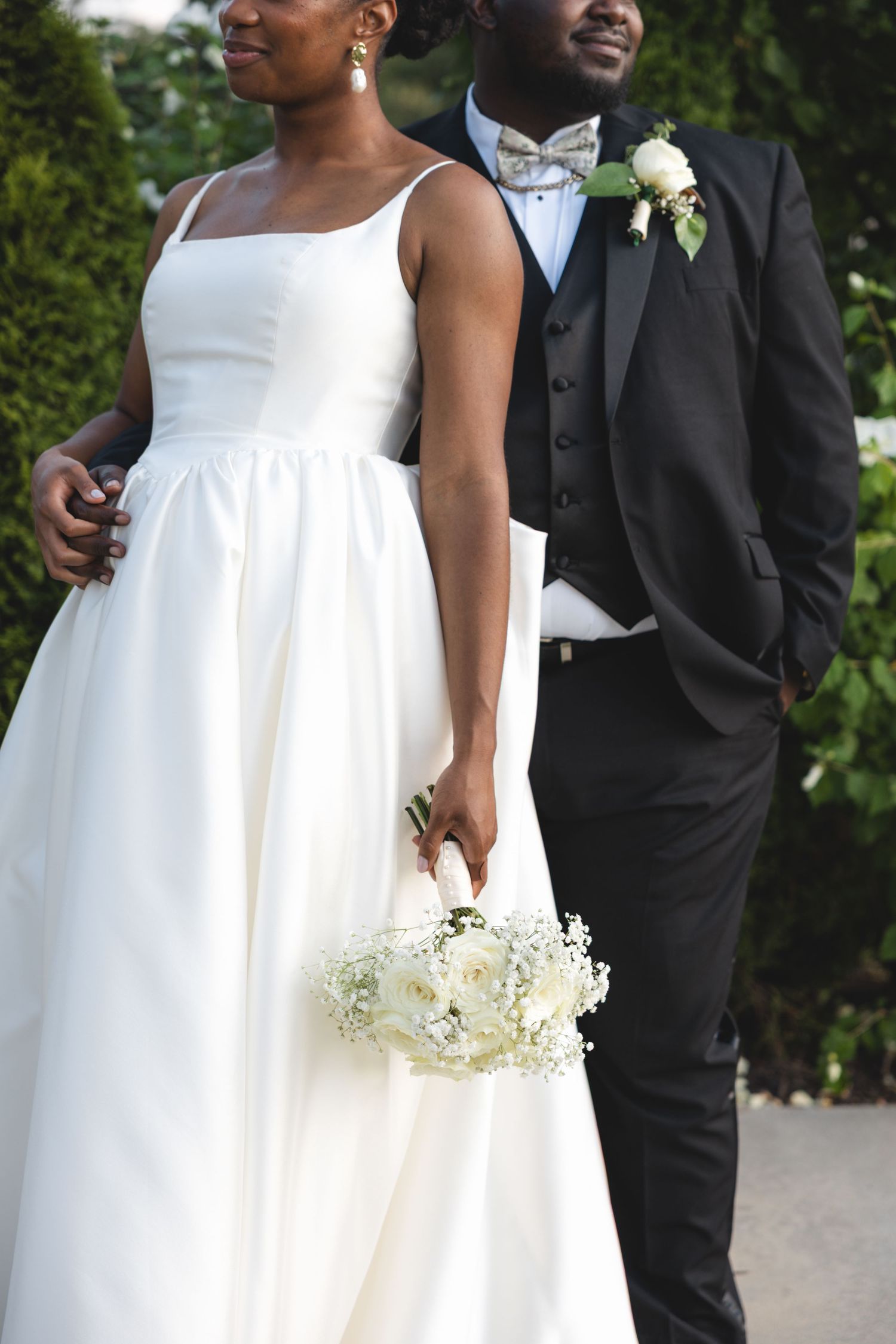 Elegant Black couple on wedding day, bride in white gown holding bouquet, groom in black tuxedo with boutonniere.