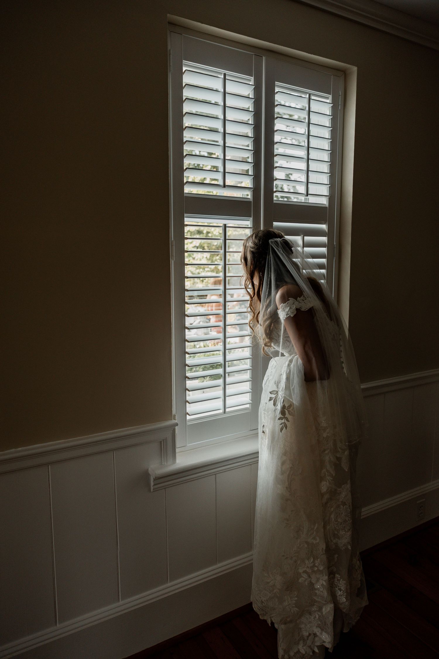 Artistic silhouette of a wedding dress against plantation shutters in natural light.