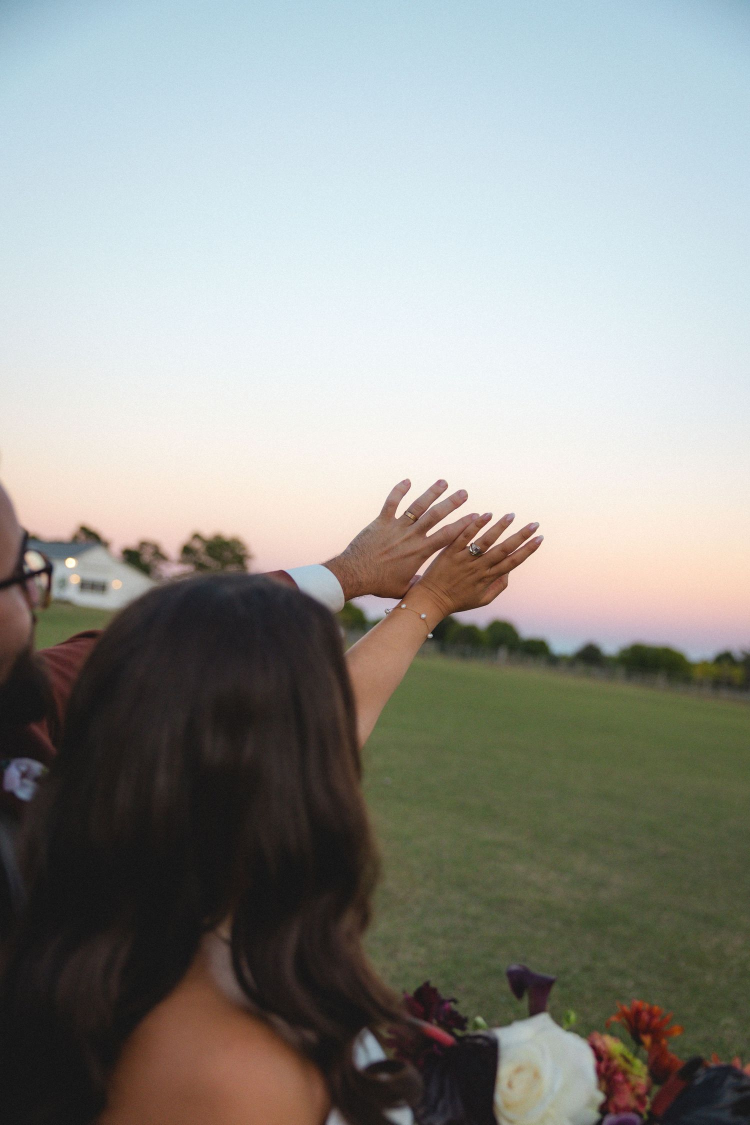Bride raising her hand with wedding ring at sunset during outdoor wedding reception on green lawn.