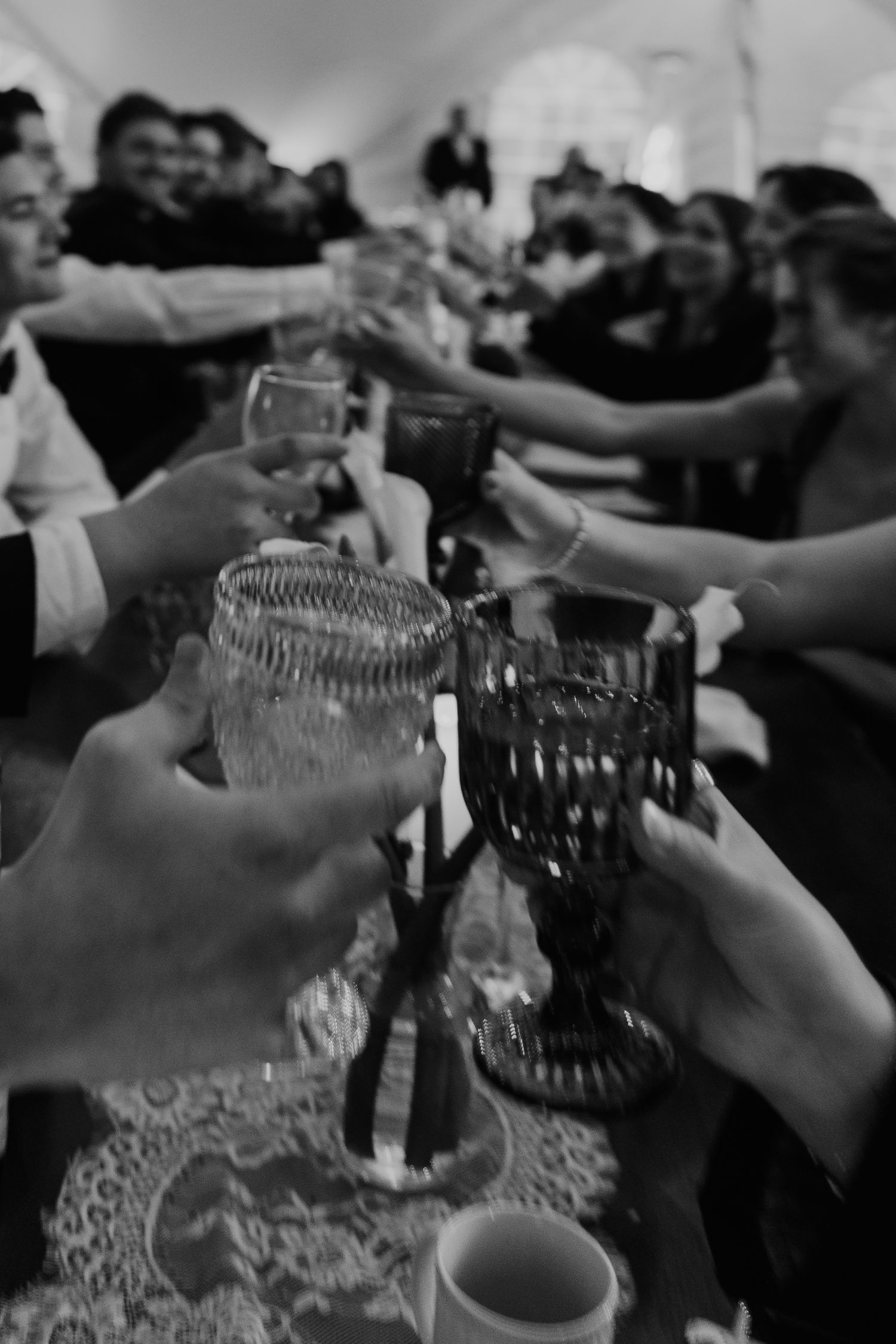 Black and white photo of wedding guests raising glasses in a celebratory toast at a tented reception.