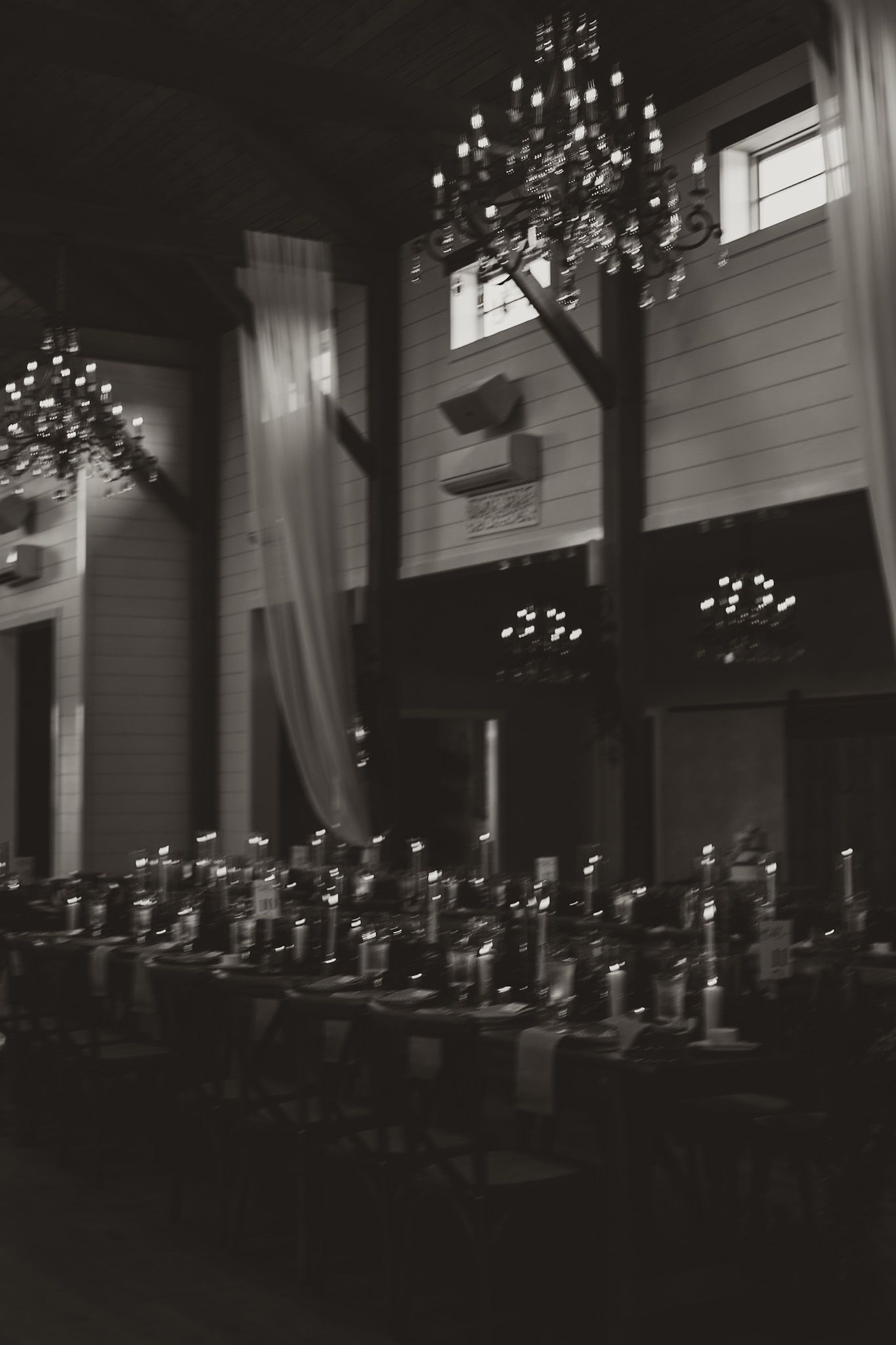 Moody black and white photo of an elegant reception venue with glowing chandeliers.