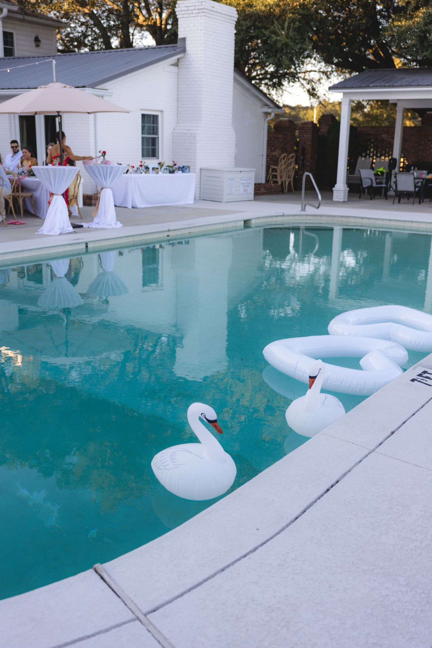 White swan pool floats in a backyard swimming pool during an elegant outdoor party event.