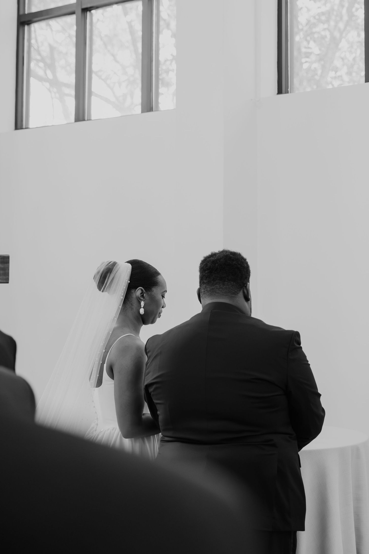 Black and white photo of a bride in veil and groom in suit standing together during wedding ceremony.