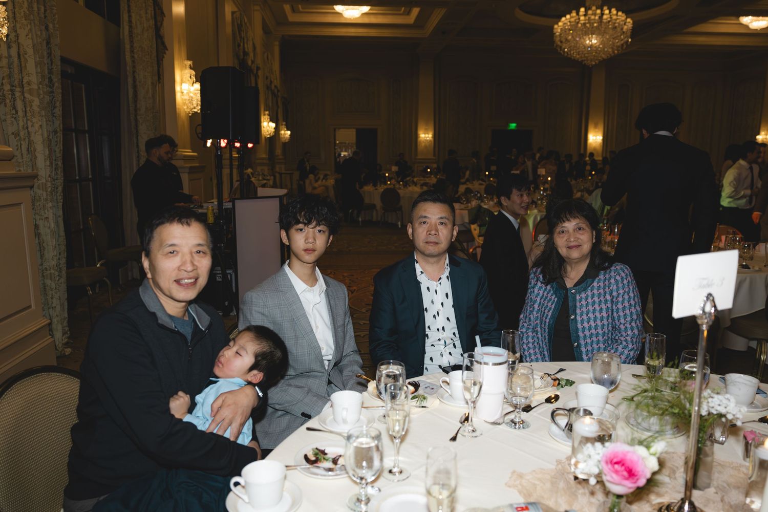 Family group posing together at wedding reception table with floral centerpiece.