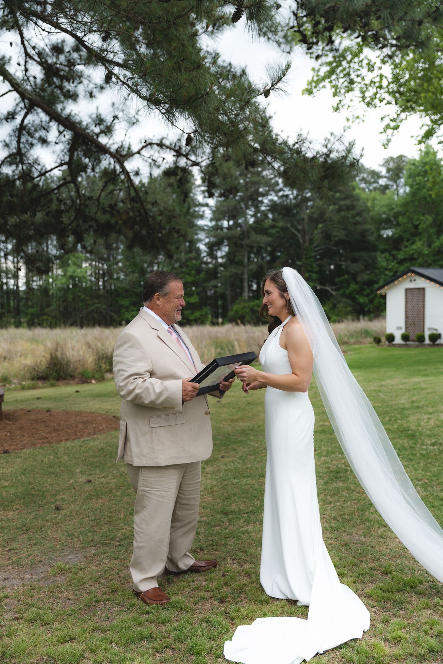 Bride in white gown and cathedral veil sharing a joyful moment with officiant during outdoor ceremony.
